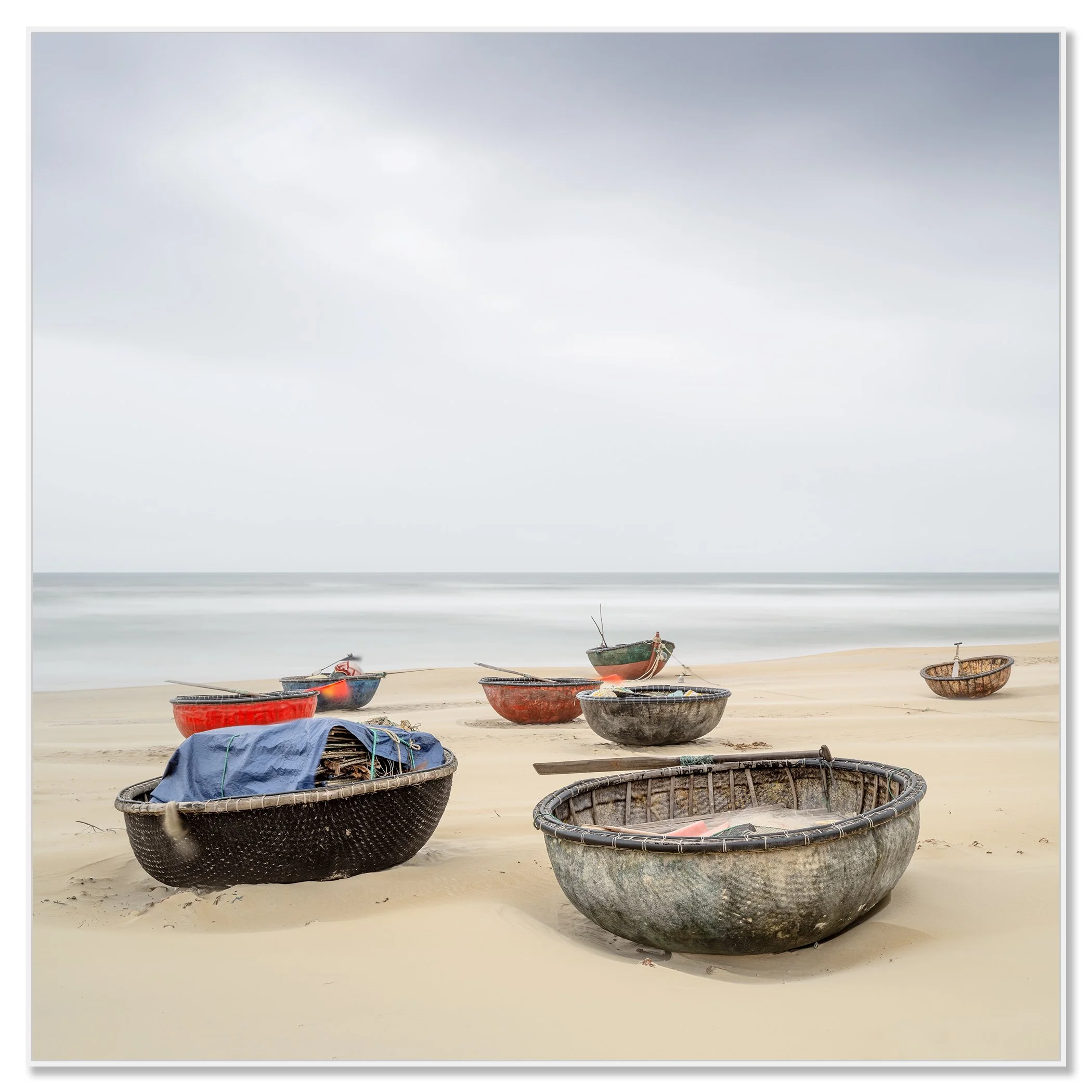 Gerald Berghammer - Color landscape photography. Several small boats resting on a sandy beach with calm ocean water under an overcast sky. Chromaluxe framed white