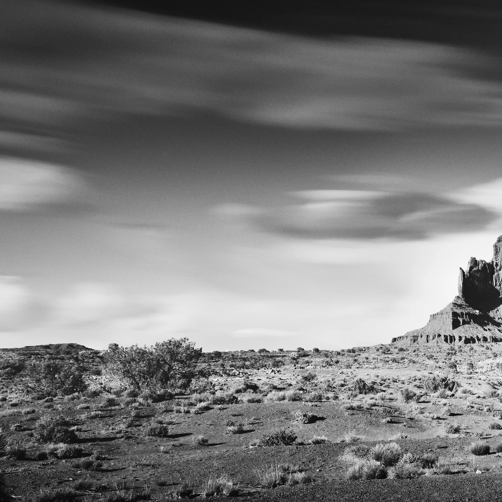© 2015 Gerald Berghammer - Black and white photography. Landscape of rugged desert terrain with large rock formations and scattered vegetation under a cloudy sky. Print detail 1