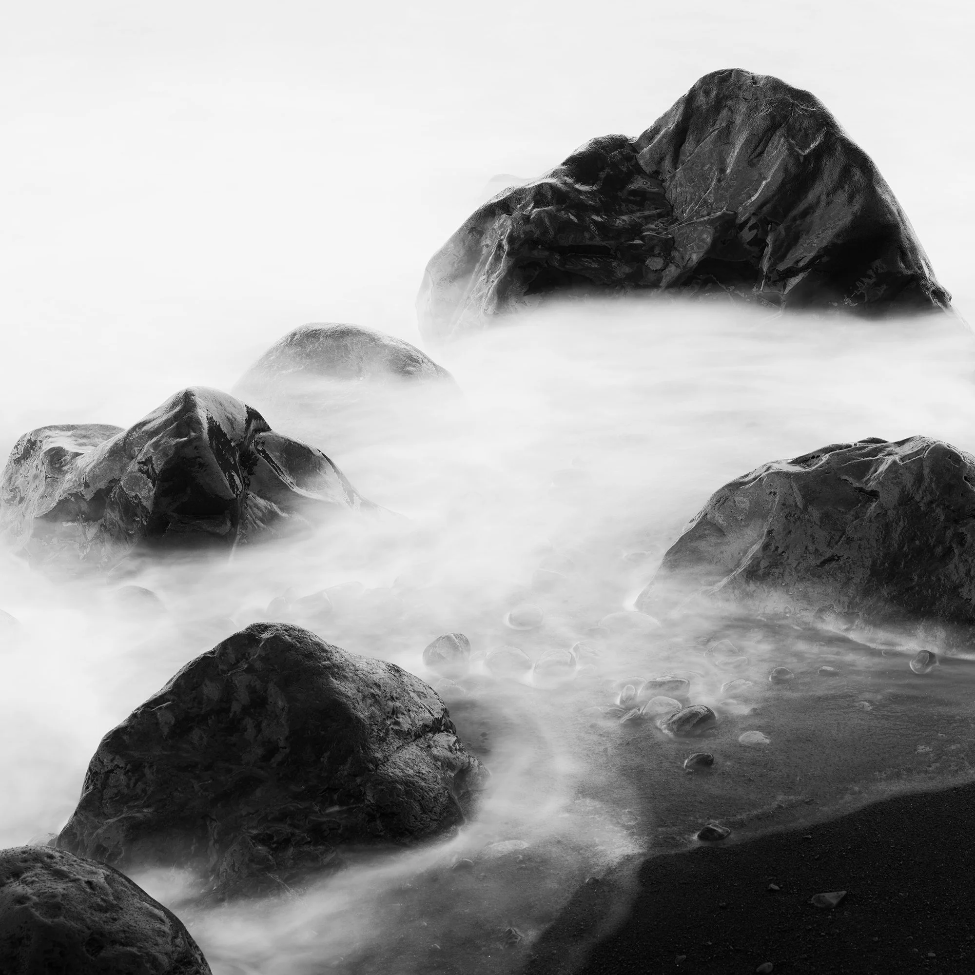 Close-up detail of Black Rocks and a Few Stones showing misty water and dark volcanic rock texture.
