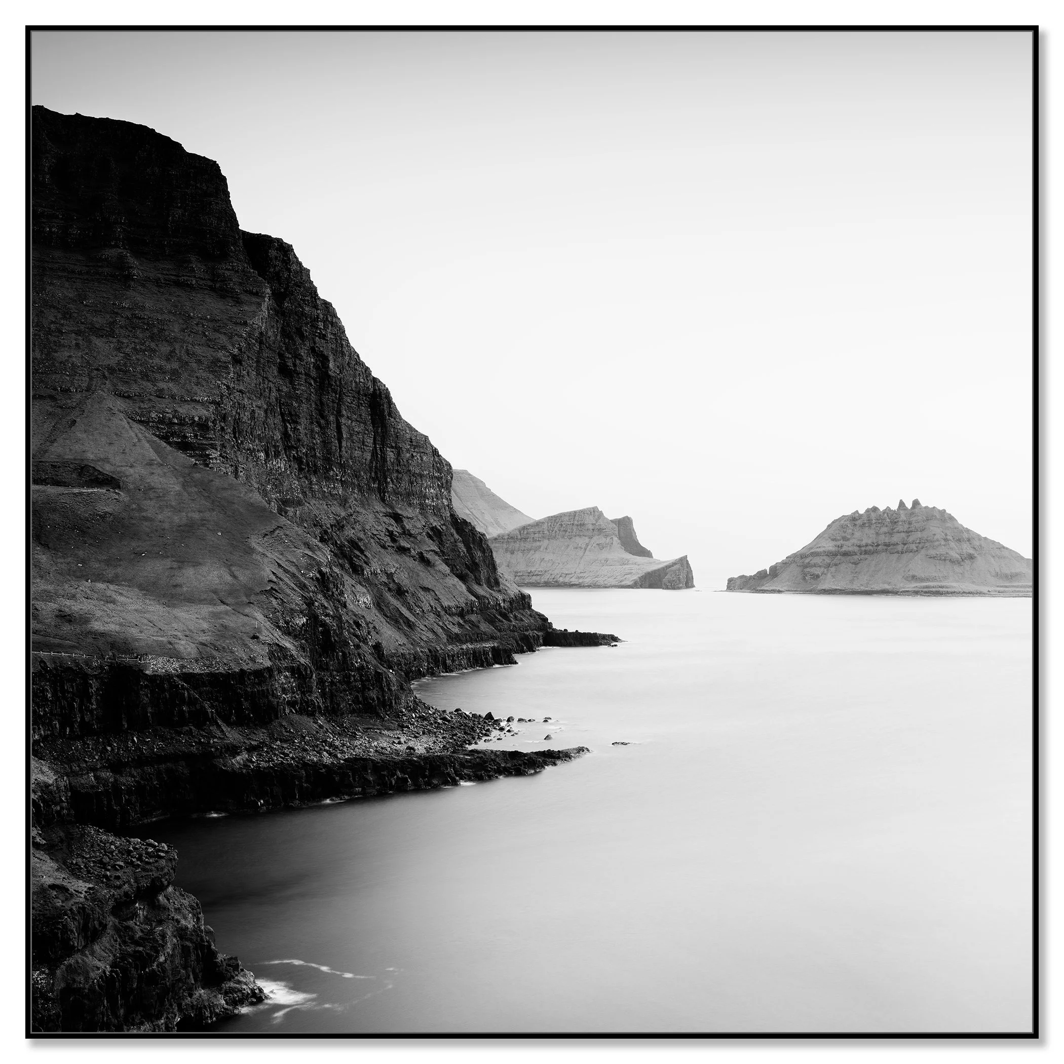 Black and white coastal landscape with steep cliffs, calm sea and distant rocky islands – framed ArtBox black