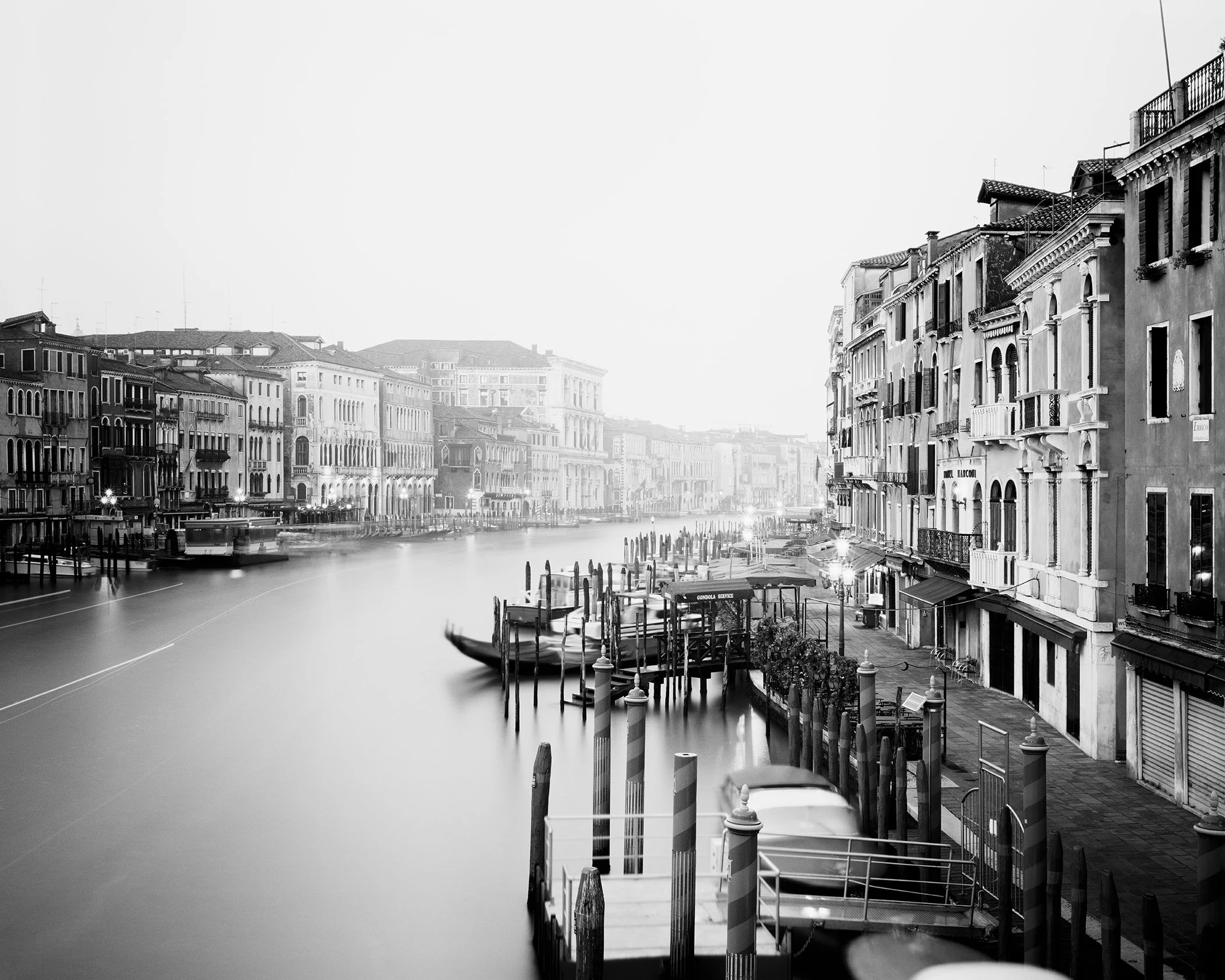 Black-and-white long-exposure photograph of Venice’s Grand Canal with gondolas and historic palazzi. Photo by Gerald Berghammer.