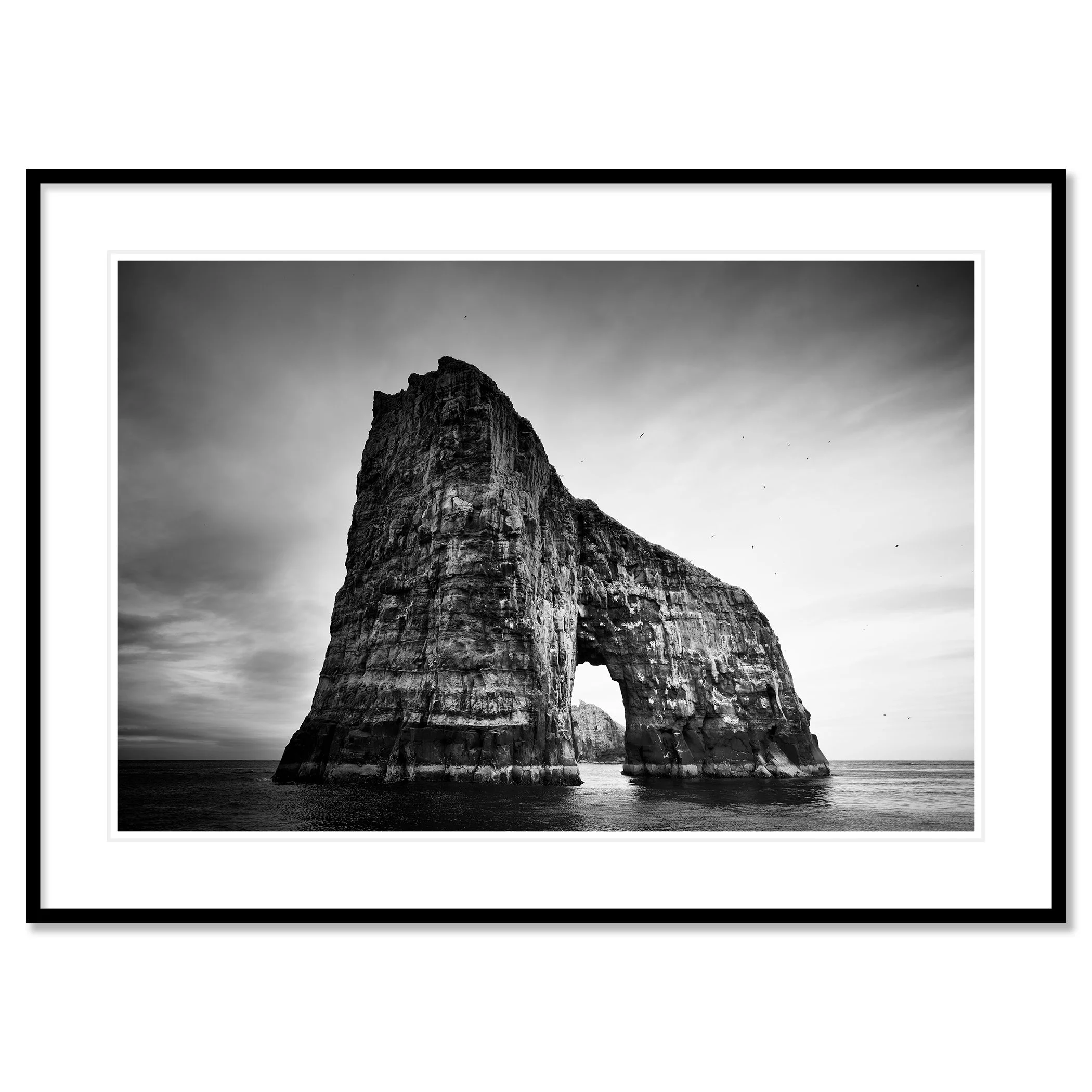 Gerald Berghammer - Black and white seascape photography.  Large natural rock formation with an arch in the middle, surrounded by water and a cloudy sky. Classic framed black