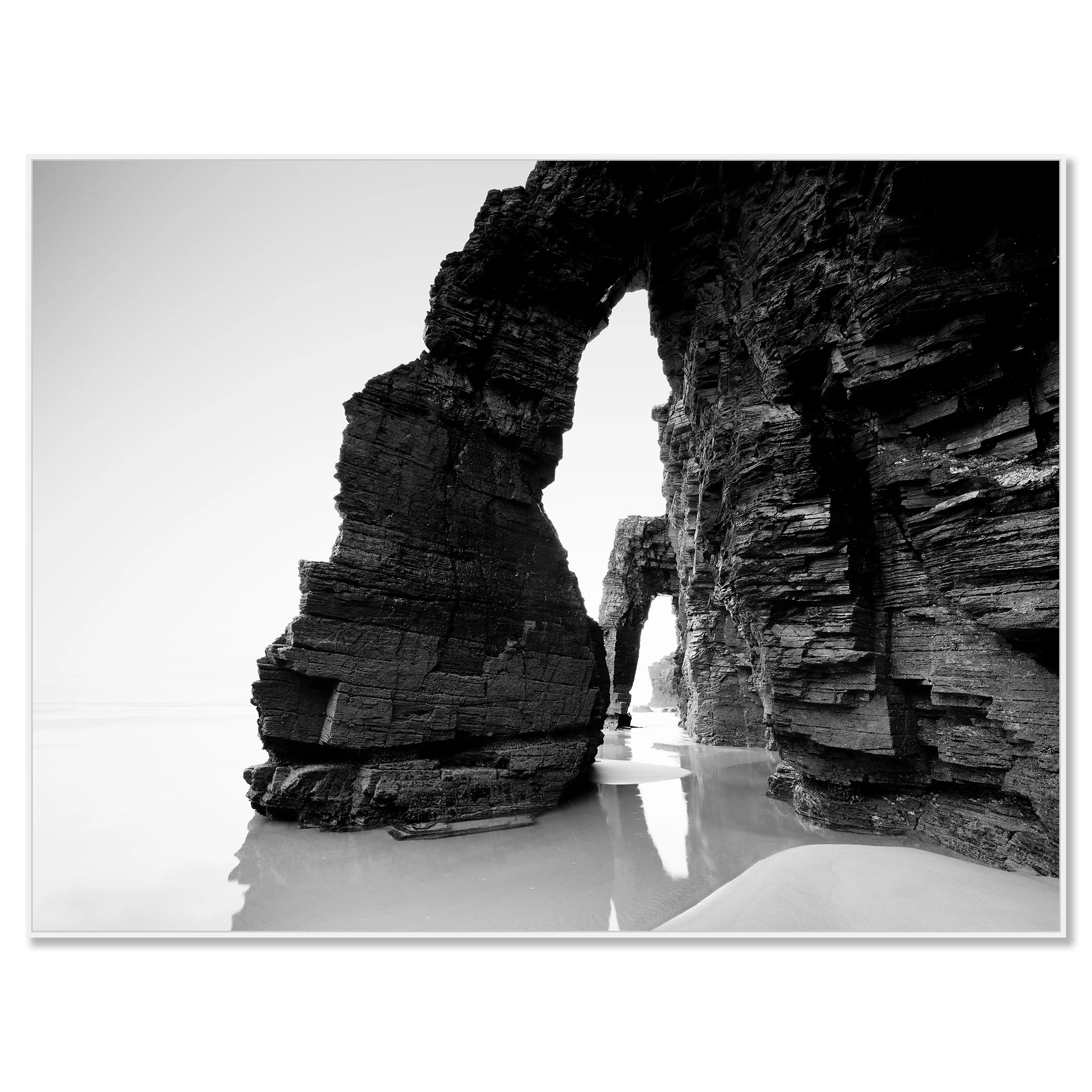 Gerald Berghammer - Black and white beach seascape photography. Large natural rock arch formations on a beach with water reflecting the rocks. Chromaluxe framed white
