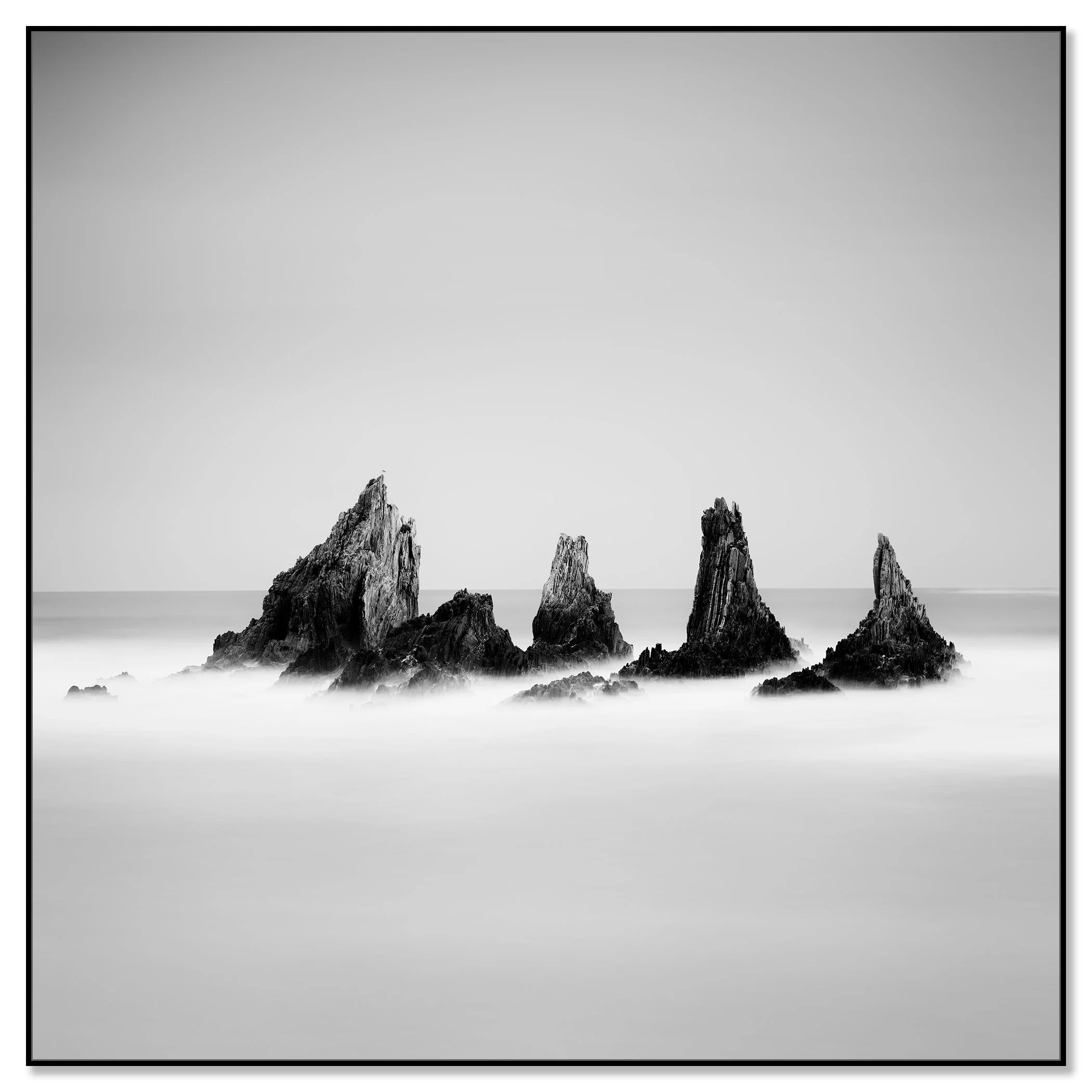 Black and white photograph of five jagged sea stacks rising from the Atlantic Ocean, with calm water and a clear sky – framed ArtBox black