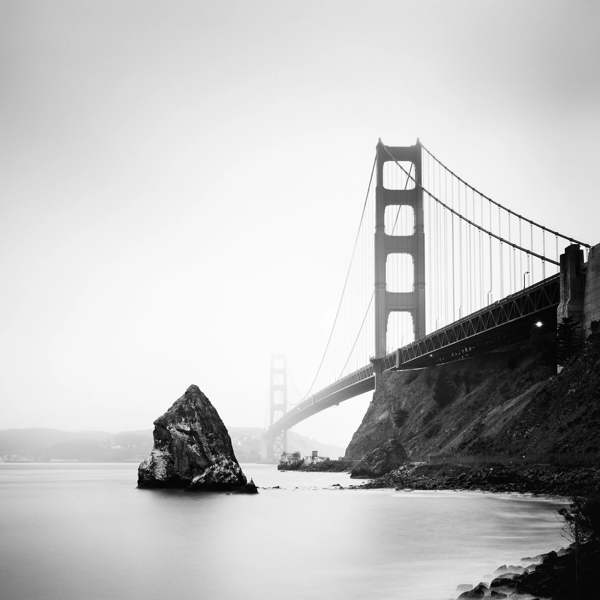 Black-and-white long-exposure photograph of the Golden Gate Bridge emerging through mist in San Francisco, California. Photo by Gerald Berghammer.