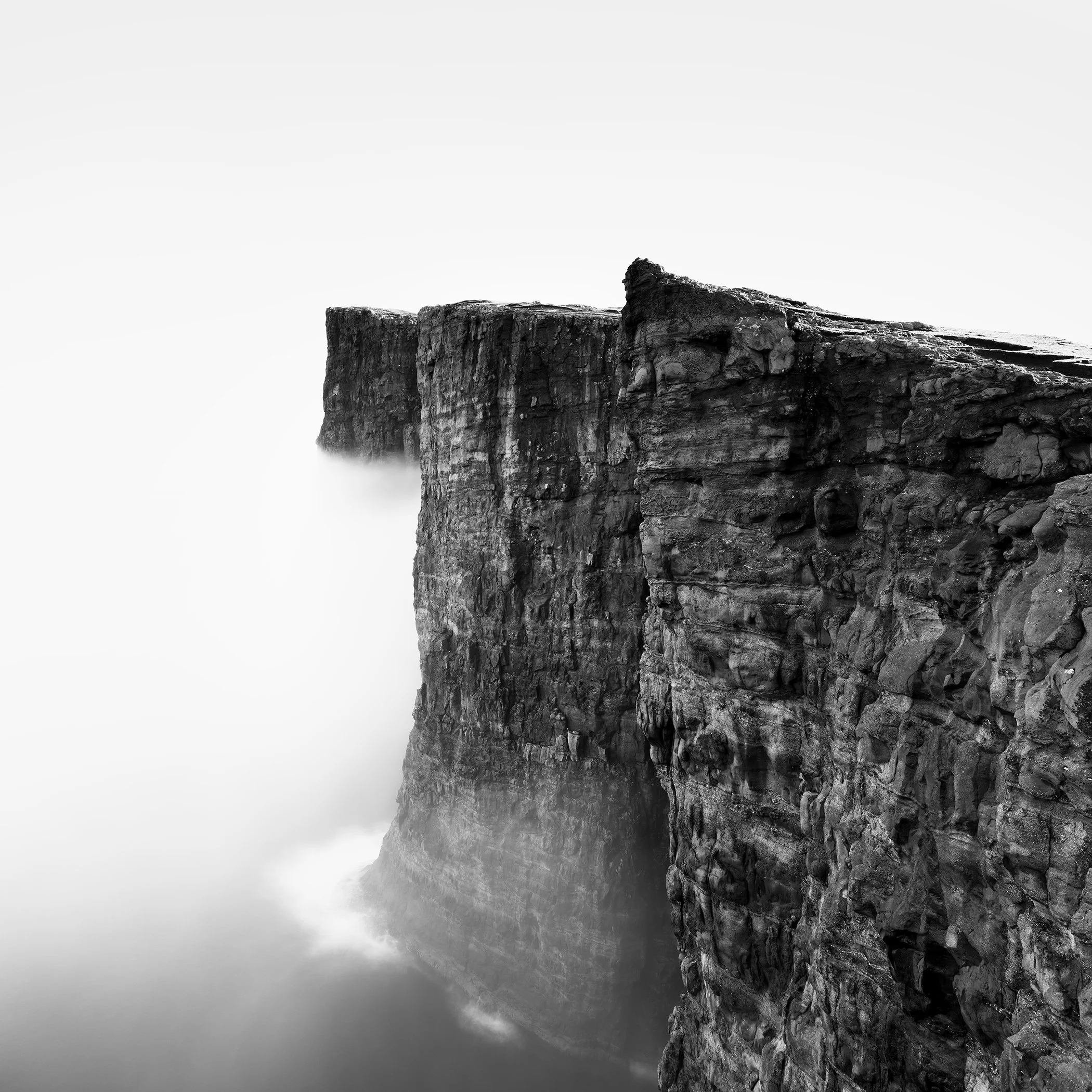 Black-and-white photograph of rugged sea cliffs emerging from mist above the ocean.
