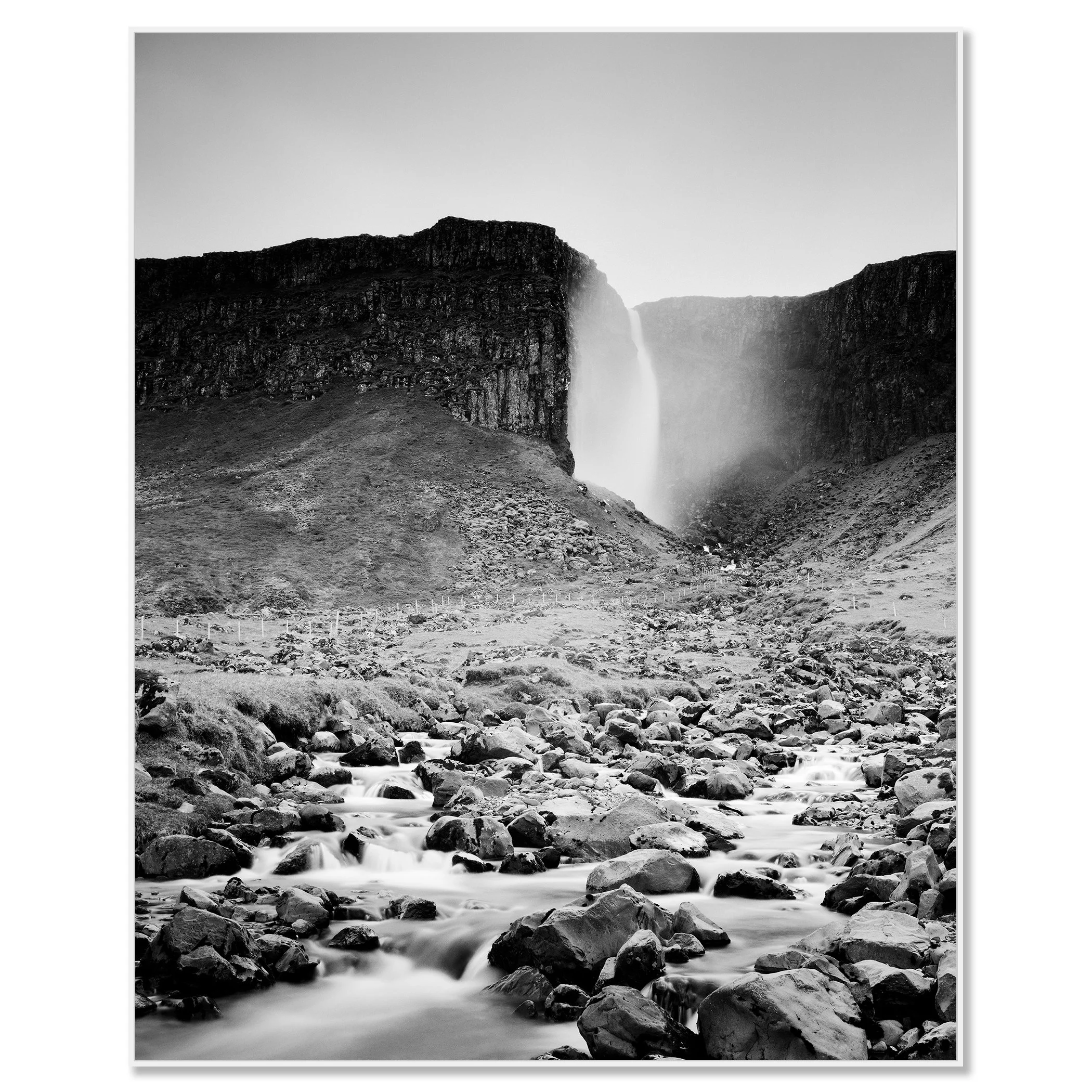 Gerald Berghammer - Black and white landscape photography. A waterfall cascading down a rocky cliff into a stream surrounded by rocks and rugged terrain. Chromaluxe framed white