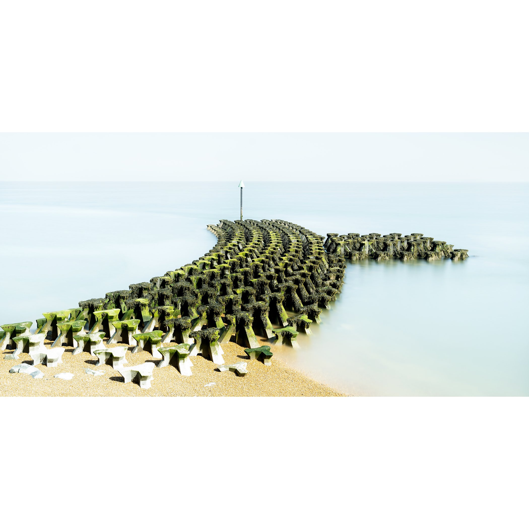 Gerald Berghammer - Color seascape panorama photography. Concrete breakwater structures on a beach extending into the water, with a pole at the end.