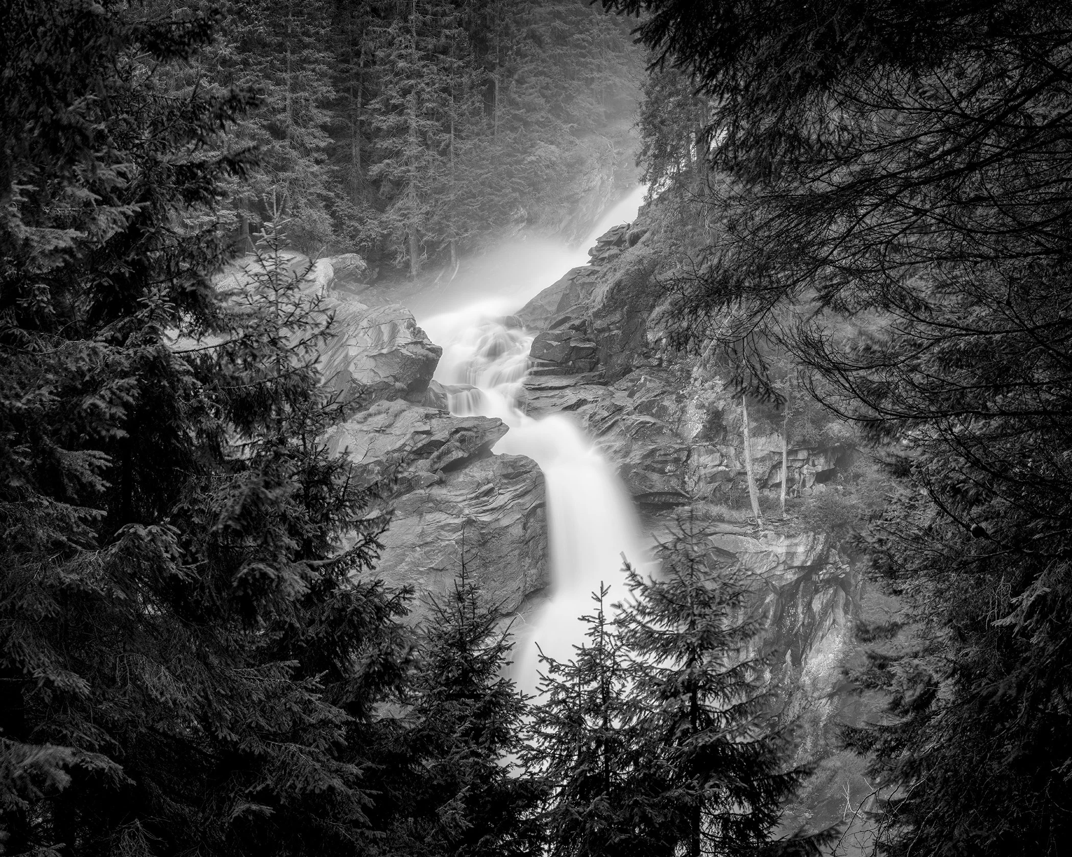 Scenic black-and-white photograph of Krimml Waterfalls surrounded by alpine woodland