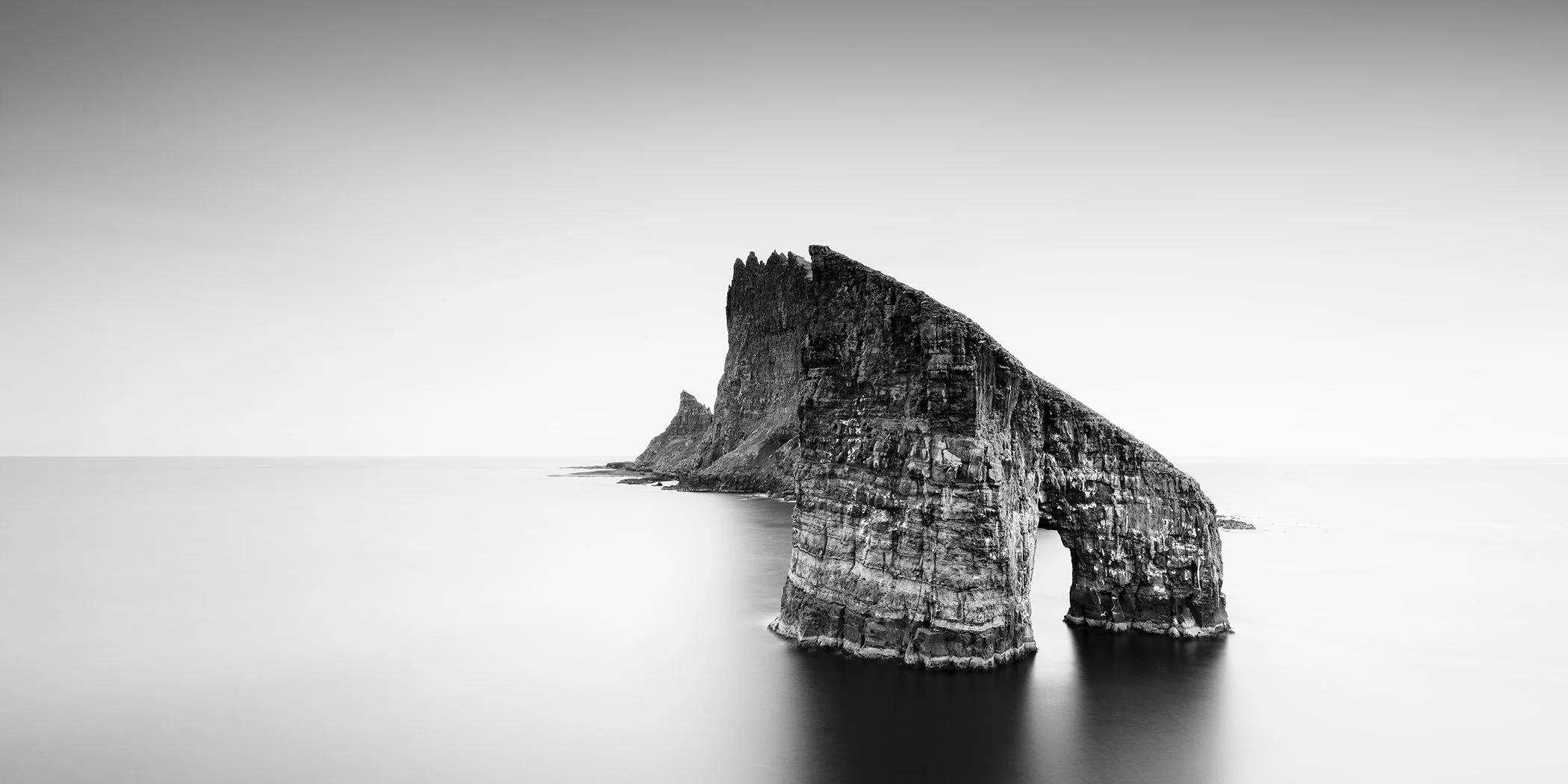 Drangarnir Sea Arch Panorama, black-and-white long-exposure photograph of the sea arch off Vágar, Faroe Islands, by Gerald Berghammer.