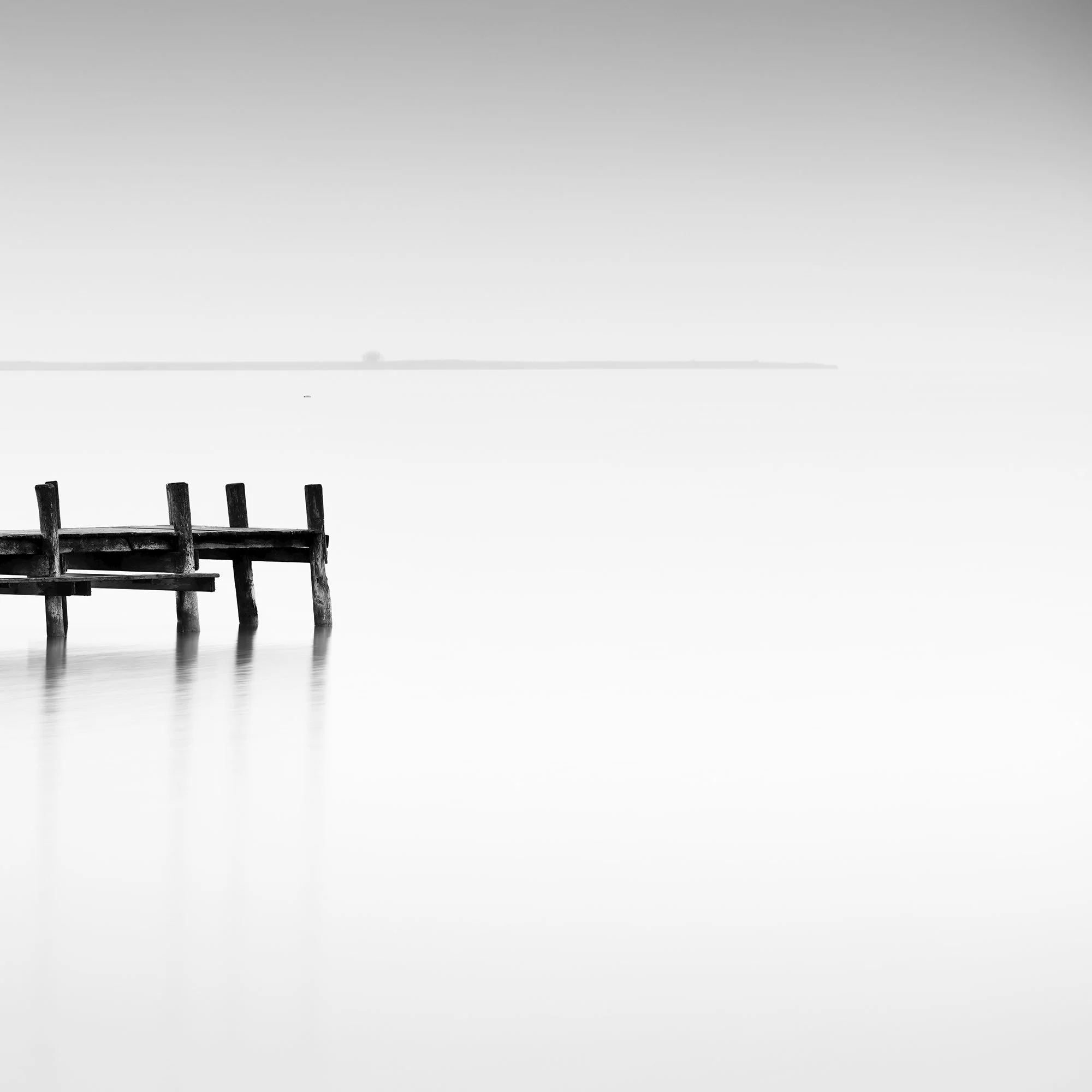 © 2023 Gerald Berghammer - Black and white long exposure waterscape photo. Wooden pier extending into calm water, with a minimalistic and serene background. Print detail 2