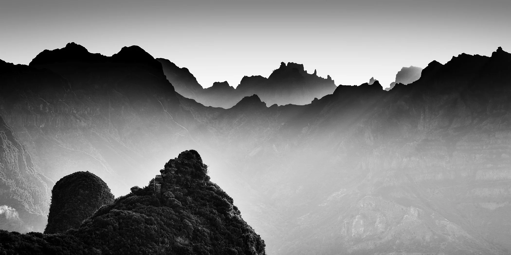 Panoramic black-and-white photograph of rugged mountain ridges emerging through mist in Madeira, Portugal. Photo by Gerald Berghammer.