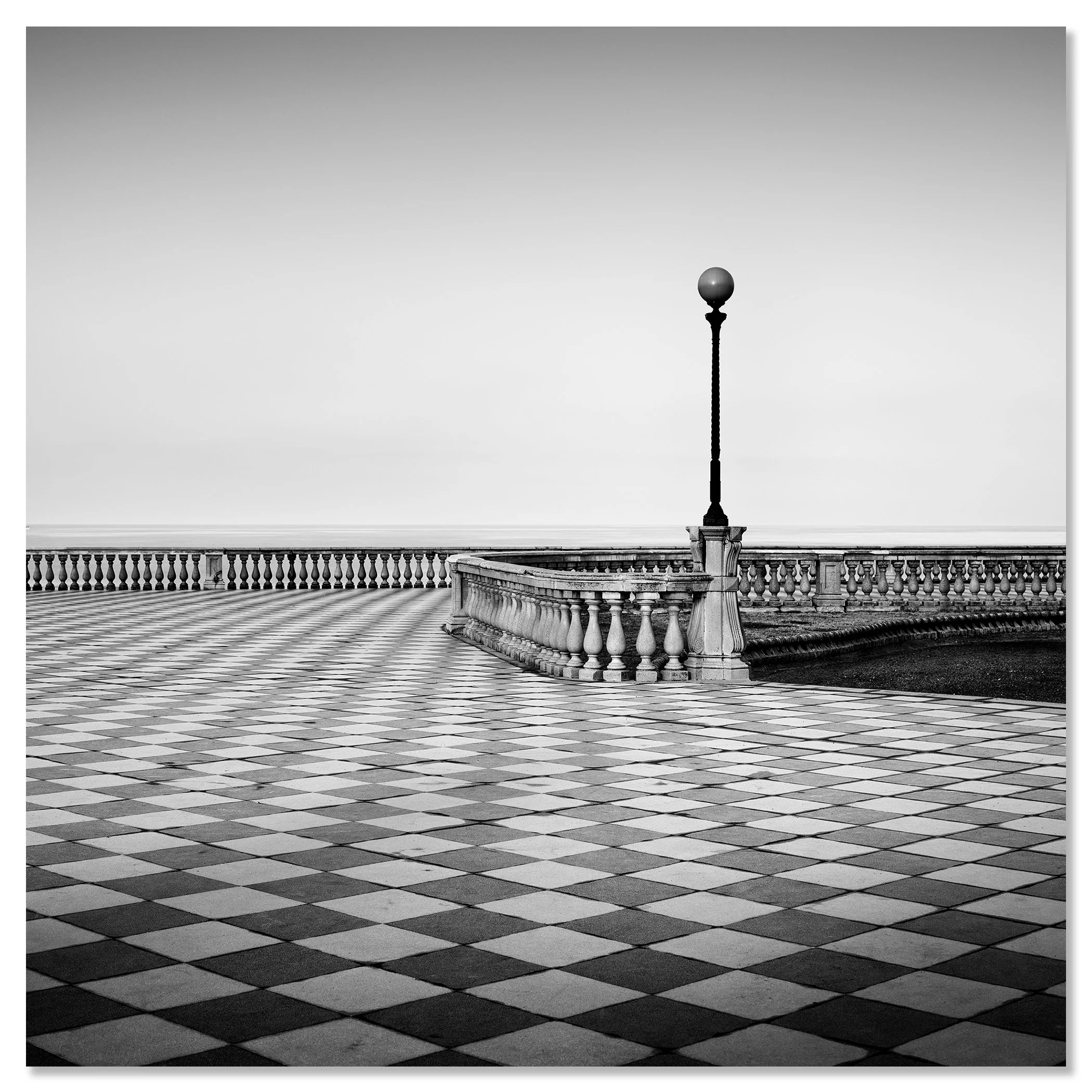 Black and white photo of an empty seaside promenade with chequerboard tiles, railings and a single lamppost – dibond frameless