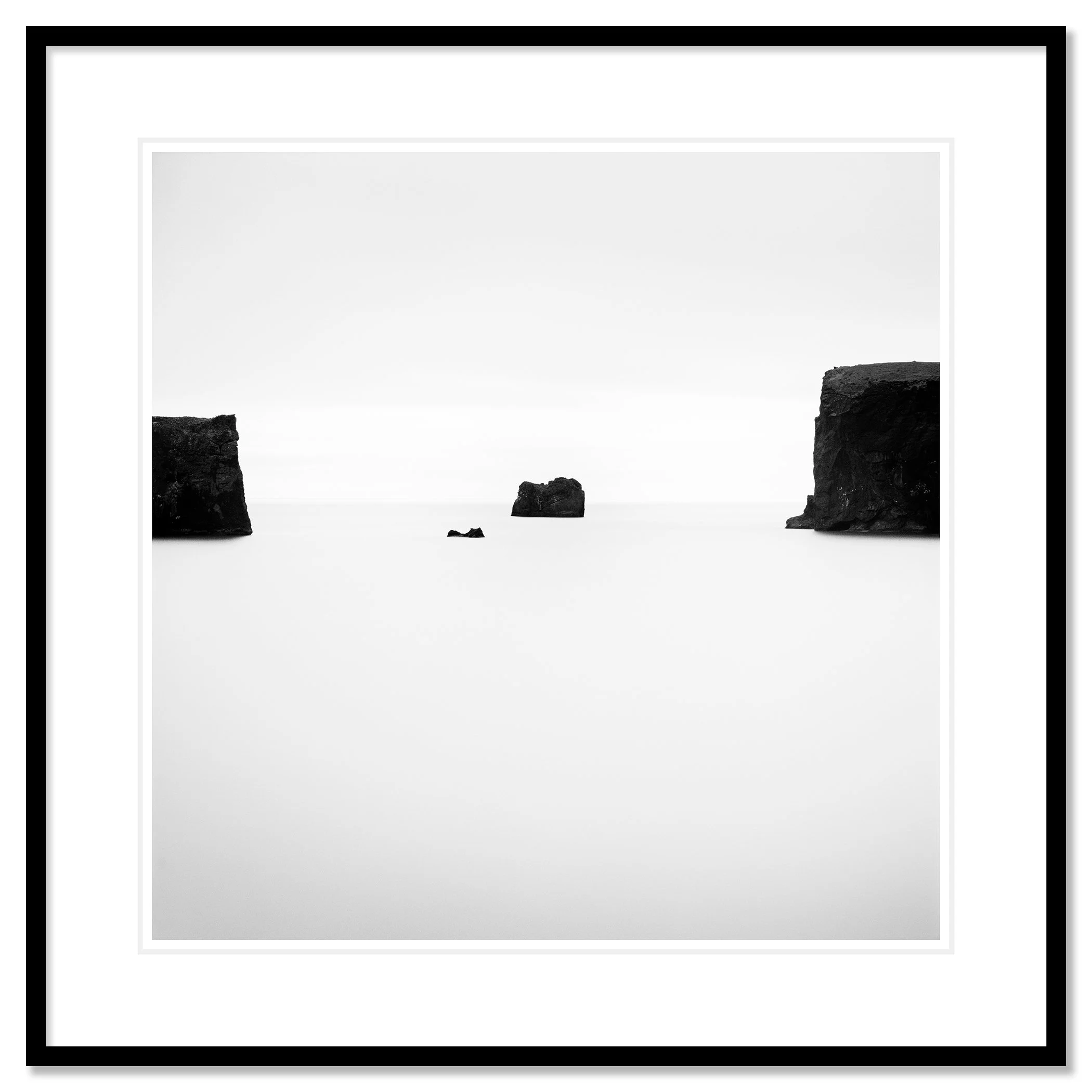 Gerald Berghammer - Black and white photo. Ocean with three rocks protruding from water, two large rocks on either side and a smaller rock in the middle. Classic framed black