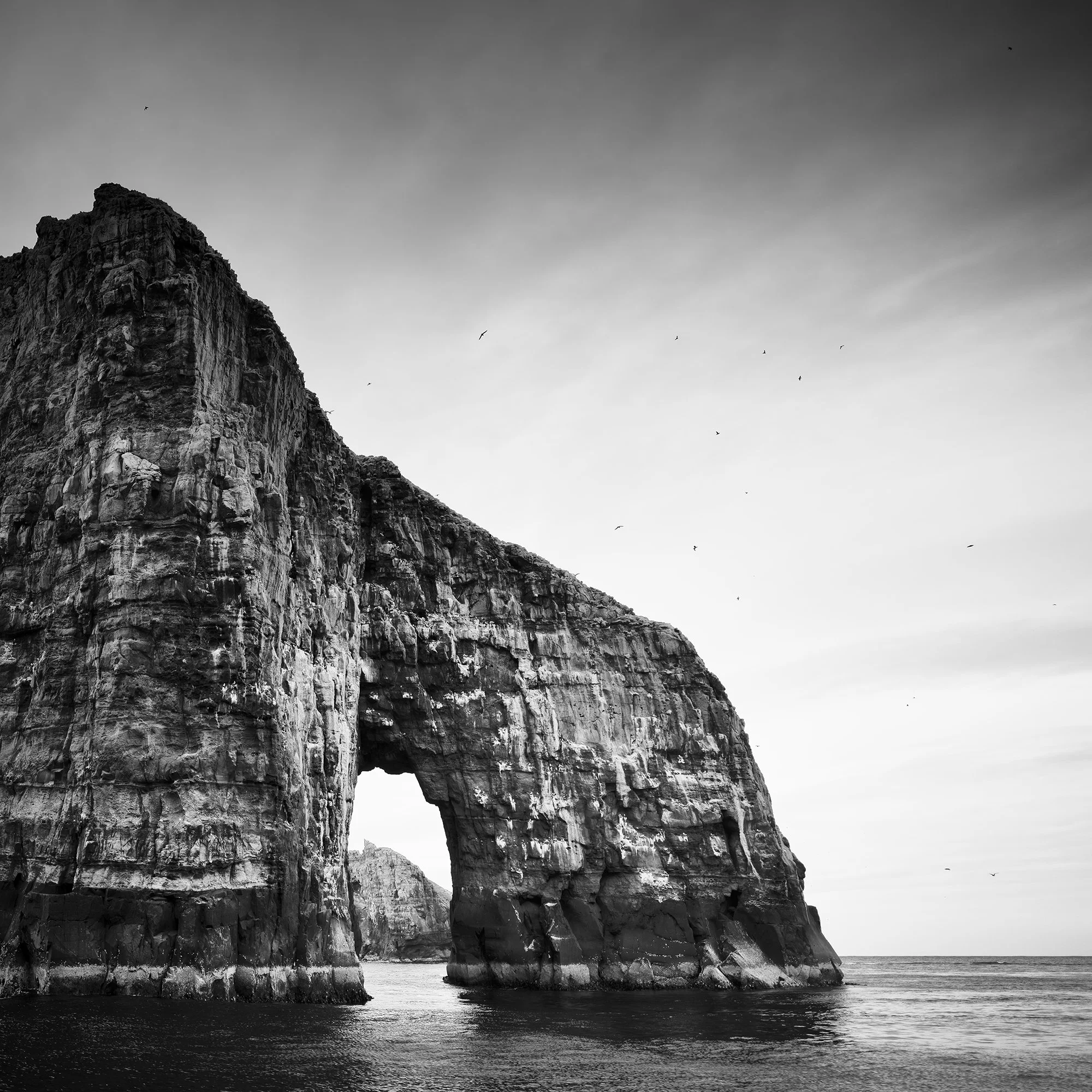 Gerald Berghammer - Black and white seascape photography.  Large natural rock formation with an arch in the middle, surrounded by water and a cloudy sky. Print detail 2