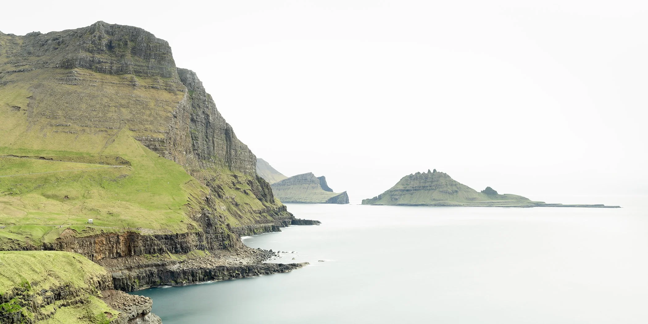 Green basalt sea cliffs descending into calm North Atlantic waters in the Faroe Islands, photographed by Gerald Berghammer.