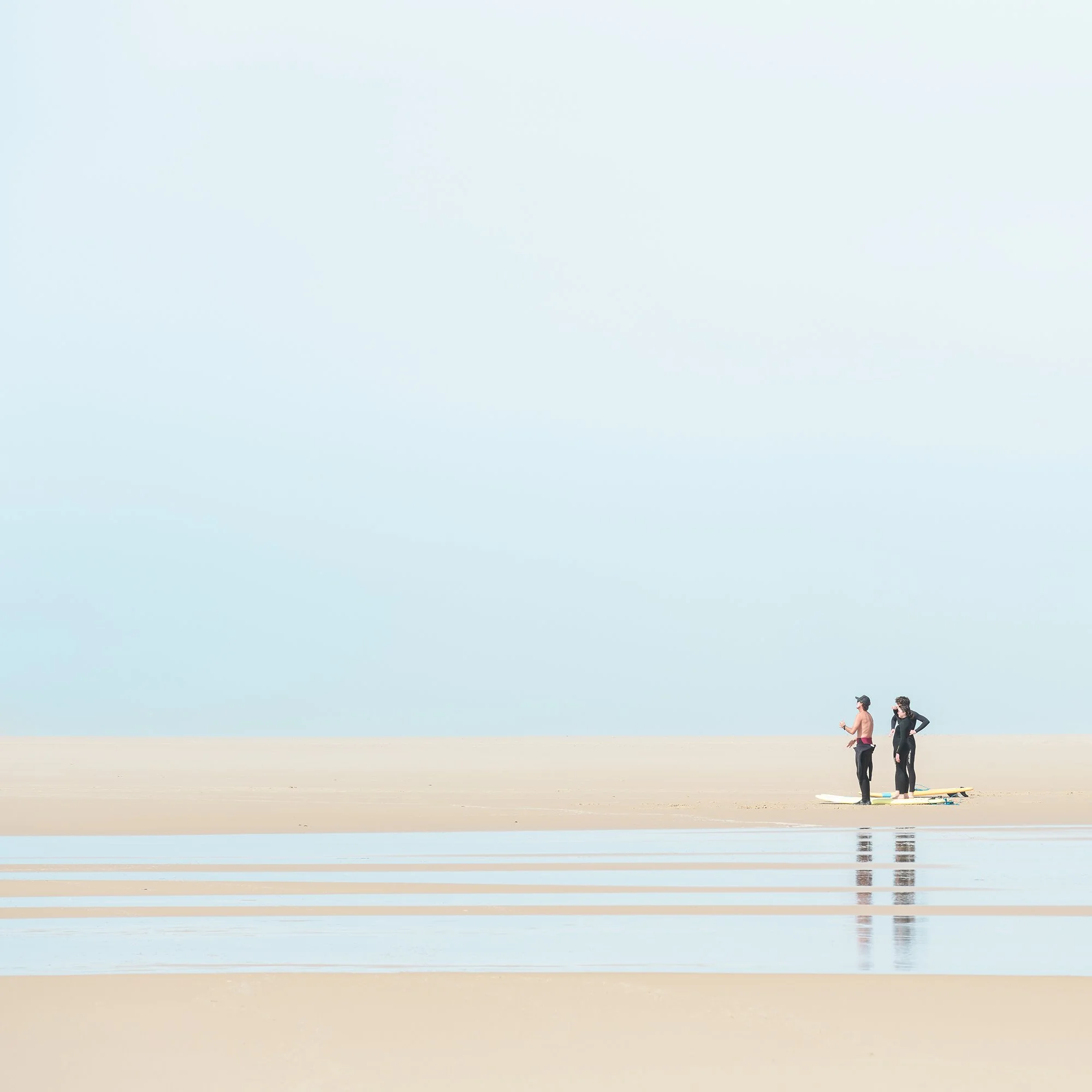 Detail of Wave Watcher, Study 1 – France, showing distant surfers on a quiet beach with shallow tidal water. Photo by Gerald Berghammer.