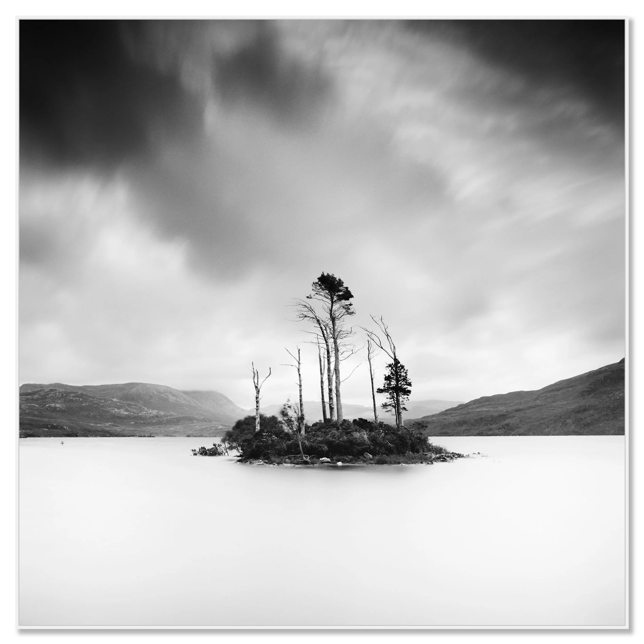 © 2012 Gerald Berghammer - Black and white waterscape photography. Small island with tall, thin trees surrounded by water and distant mountains under a cloudy sky. Chromaluxe framed white