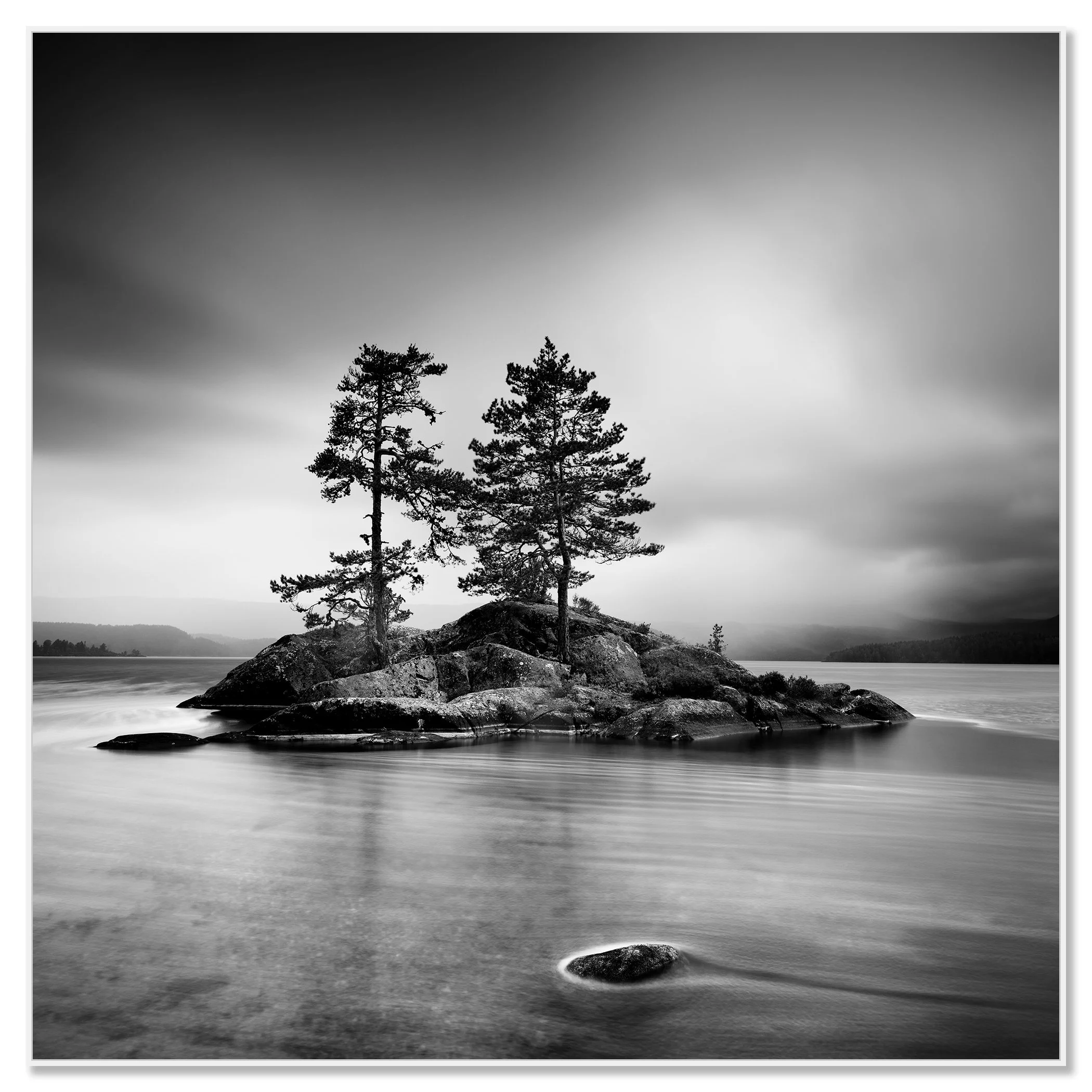 Black and white nature photograph of a rocky lake island with two pine trees and dramatic overcast skies – framed ArtBox white