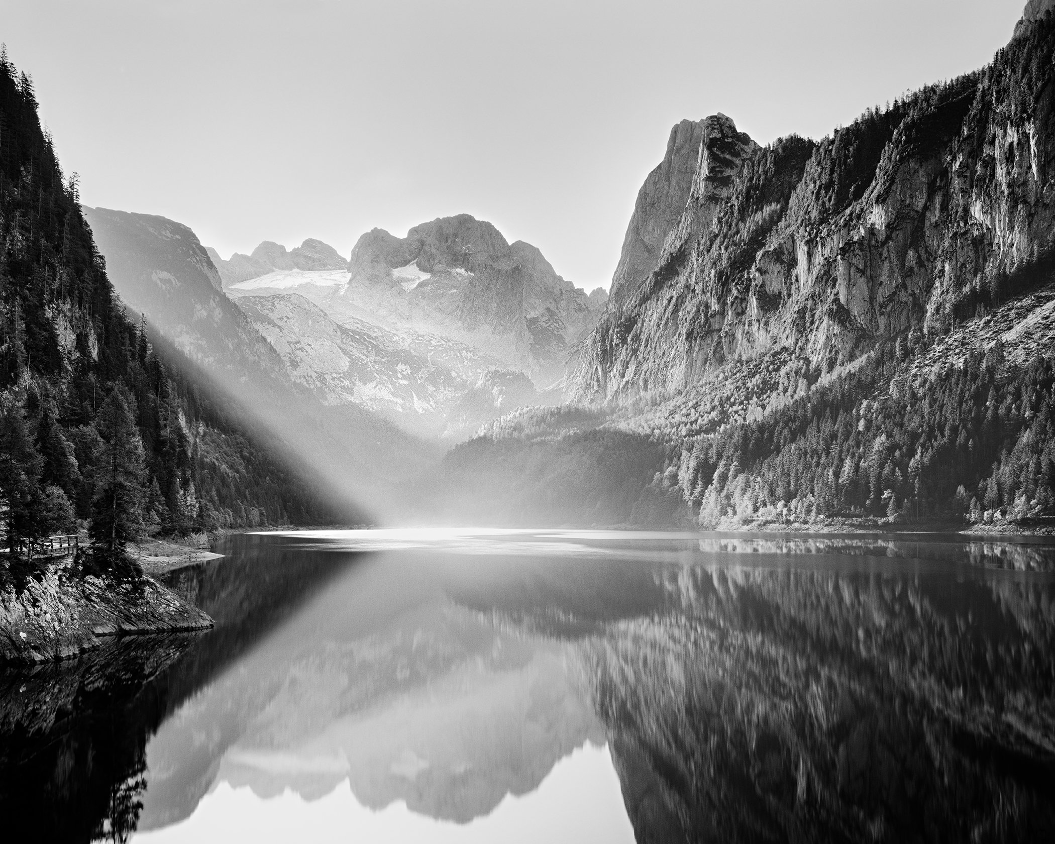 Sunlight falls across calm Lake Gosau beneath rugged peaks in the Austrian Alps, reflected in the still water. Photo by Gerald Berghammer.