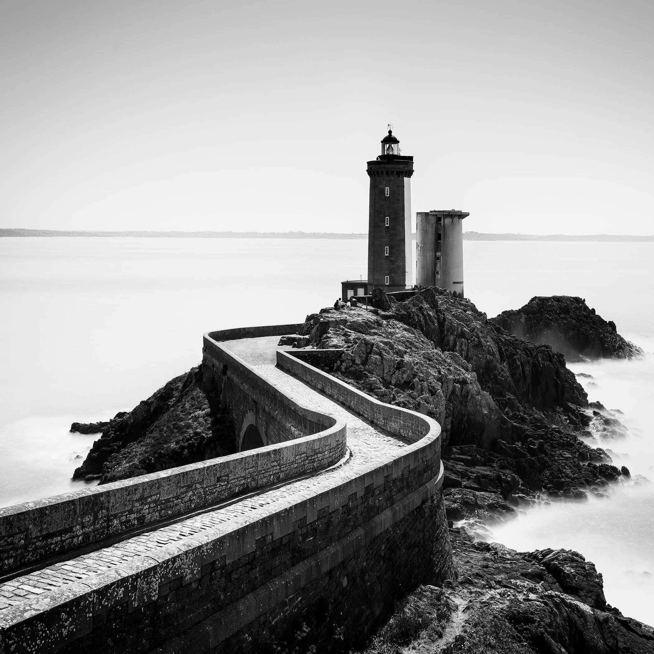 Atmospheric black-and-white seascape of Petit Minou Lighthouse in Brittany, surrounded by rocks and mist-softened water.