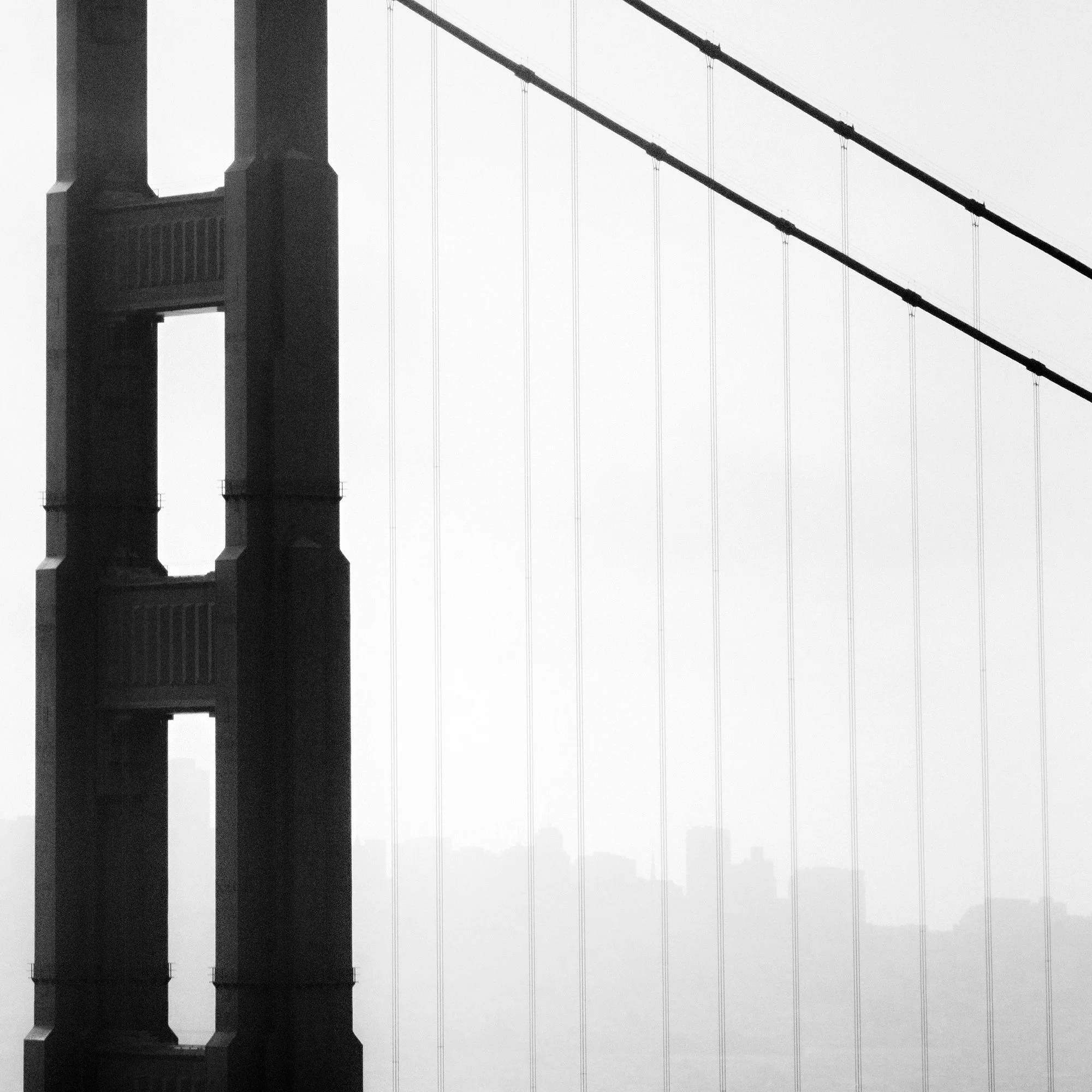© 2015 Gerald Berghammer - Black and white photo. Golden Gate Bridge in San Francisco, seen from the side, with the city skyline faintly visible in the background. Print detail 2