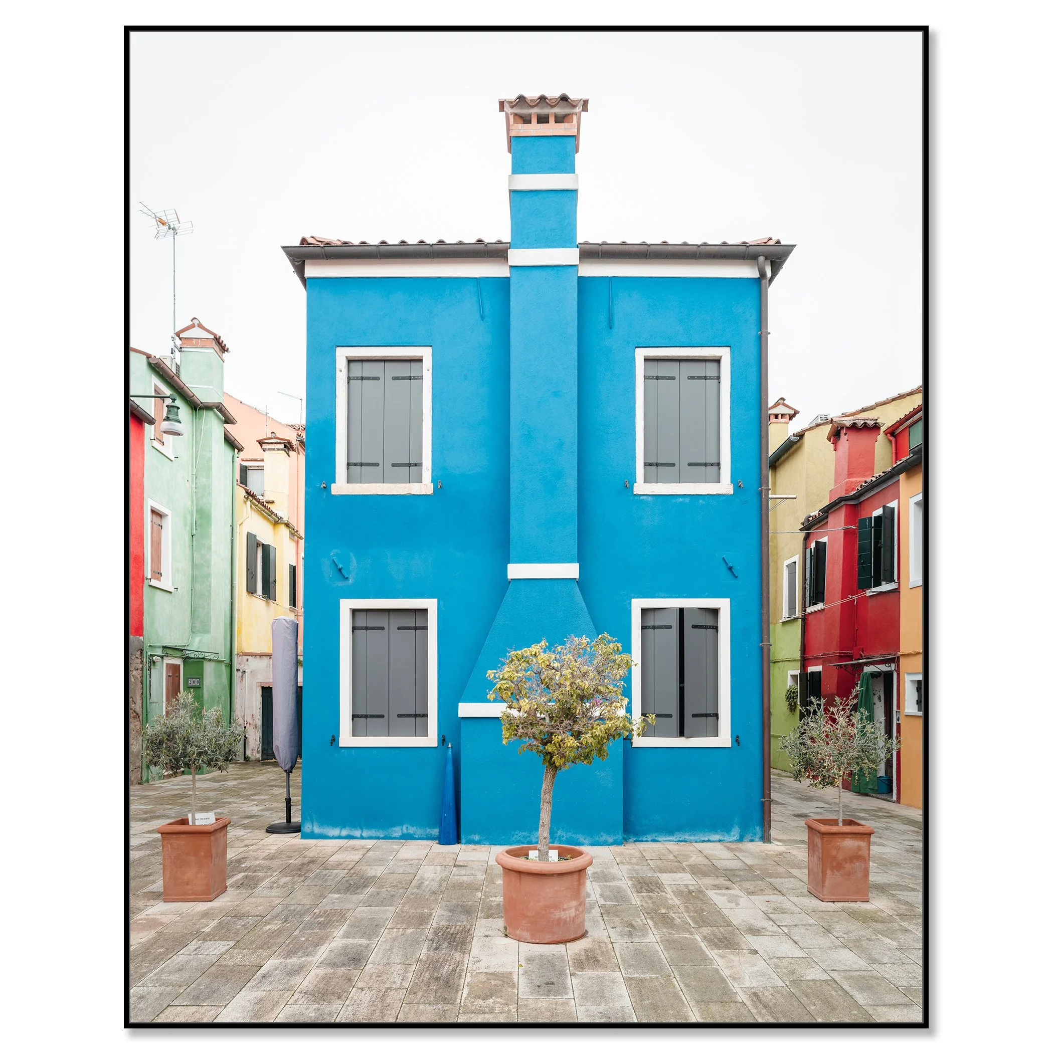 © 2025 Gerald Berghammer - Color cityscape photo. Colorful row houses with a prominent blue house in the center, potted small trees in front, and a paved courtyard. Chromaluxe framed black