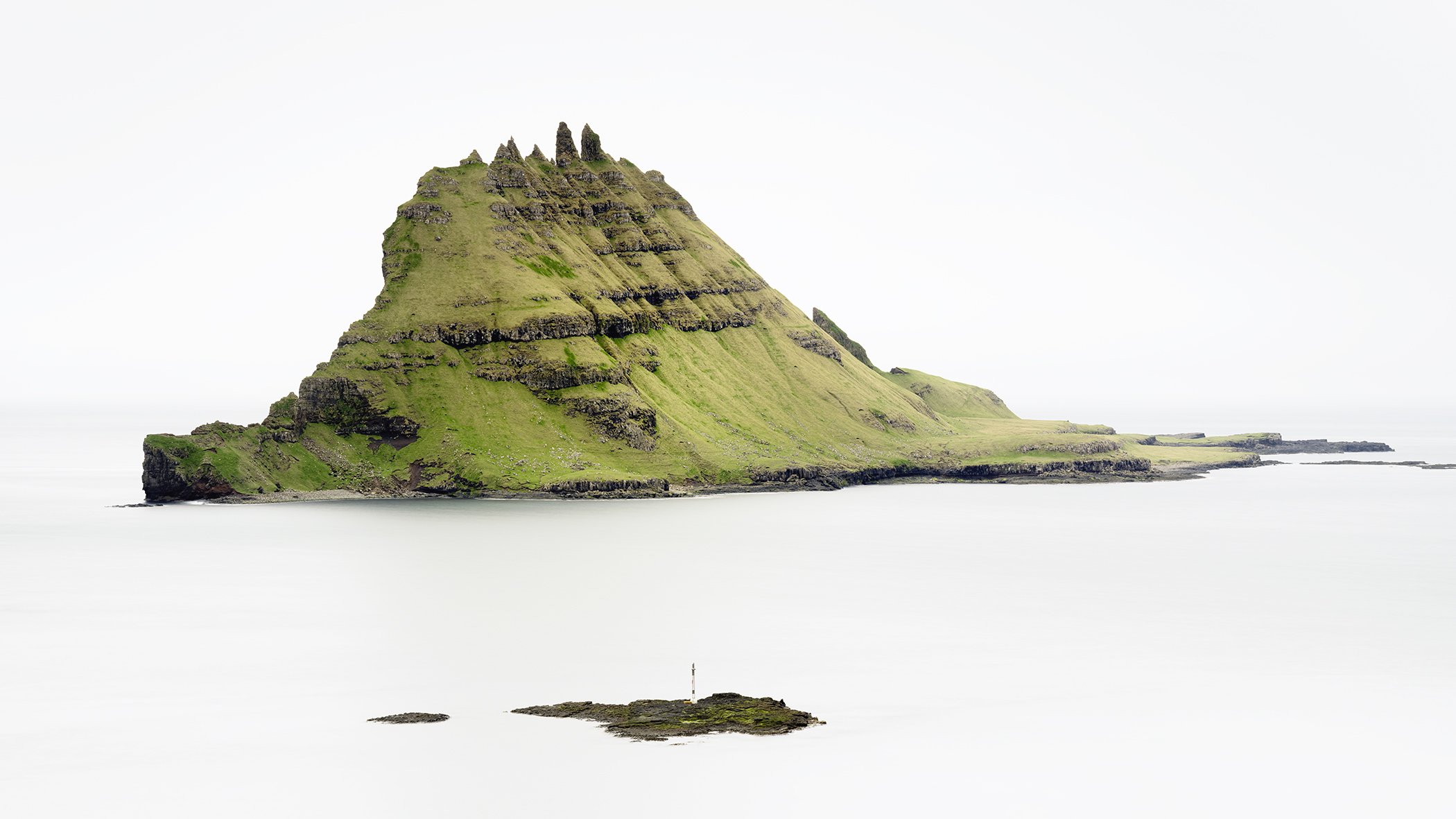 Green Rock Island – Faroe Islands, dramatic green island landscape surrounded by calm sea under an overcast sky by Gerald Berghammer
