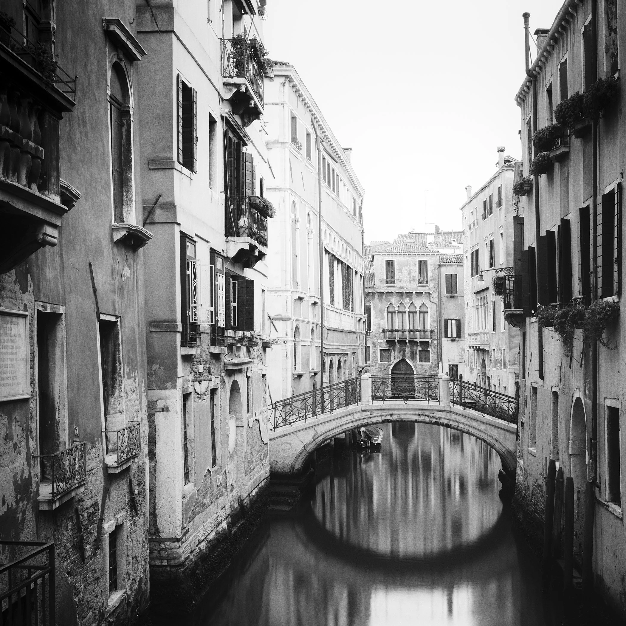 Black-and-white fine art photograph of a historic stone bridge over a quiet Venetian canal by Gerald Berghammer.