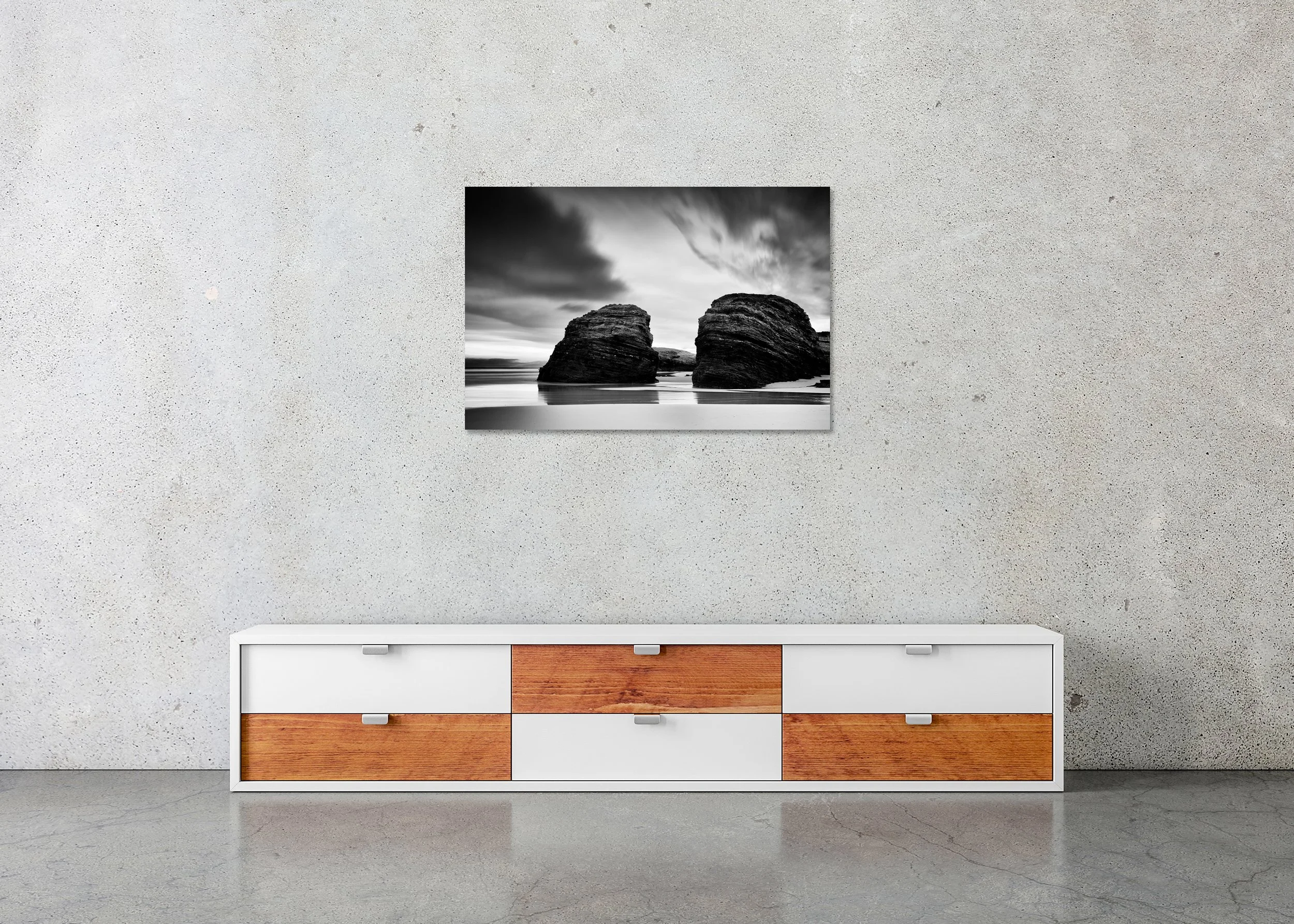Minimalist black-and-white coastal landscape photograph of two large rounded rocks on the shoreline under a cloudy sky with the sea behind on a frameless ChromaLuxe metal print