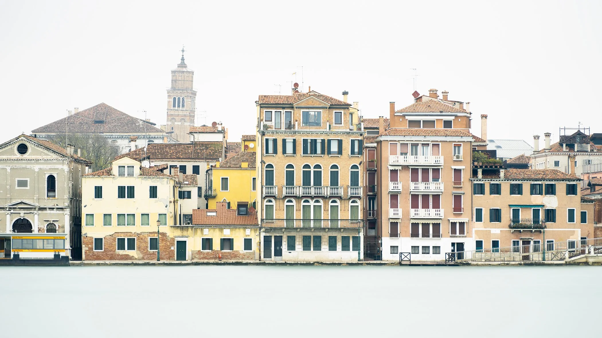 Minimalist colour photograph of historic Venetian façades and terracotta rooftops along the lagoon in Venice, Italy. Photo by Gerald Berghammer.
