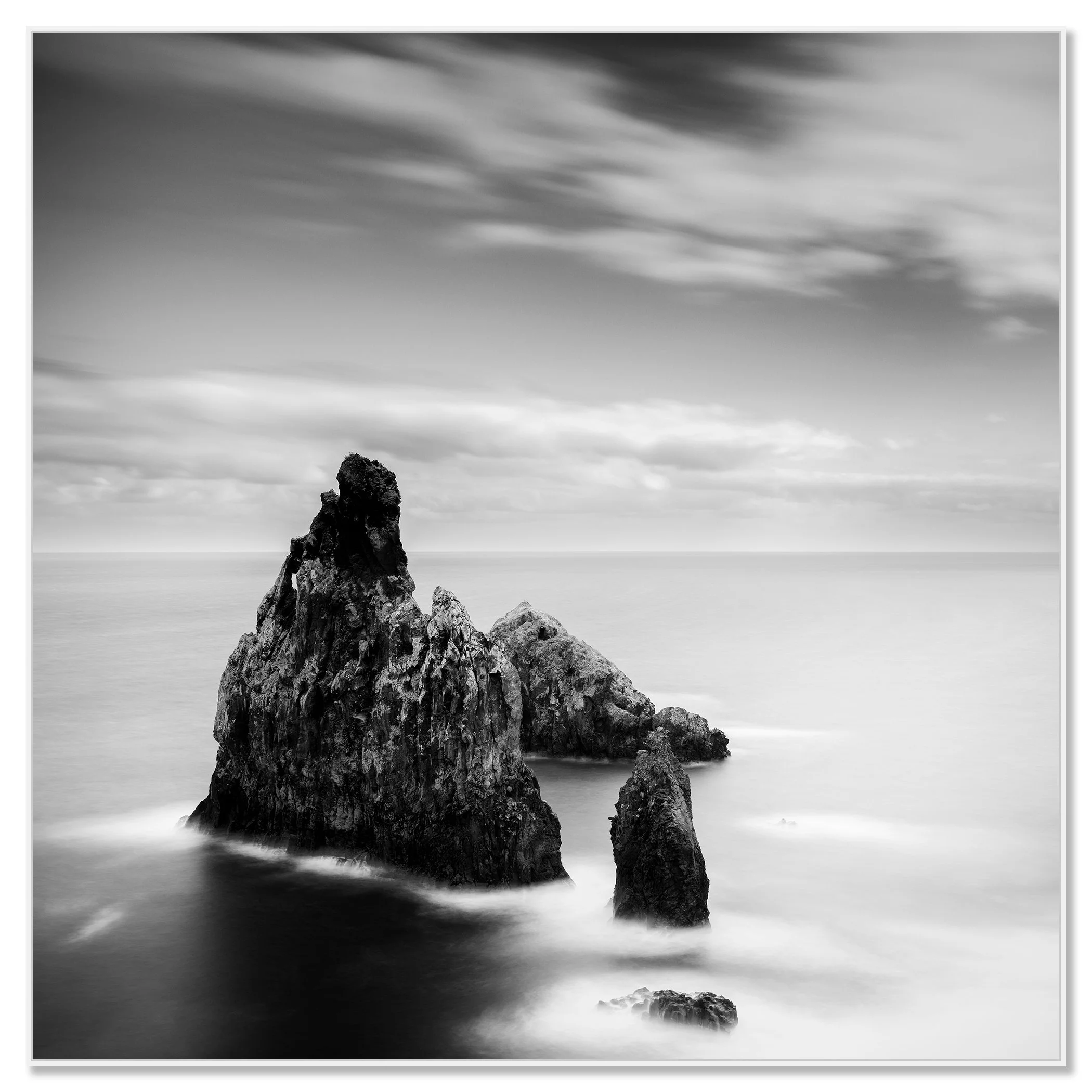 Three large rocks rising from the sea close to the shore under an overcast sky – framed ArtBox white
