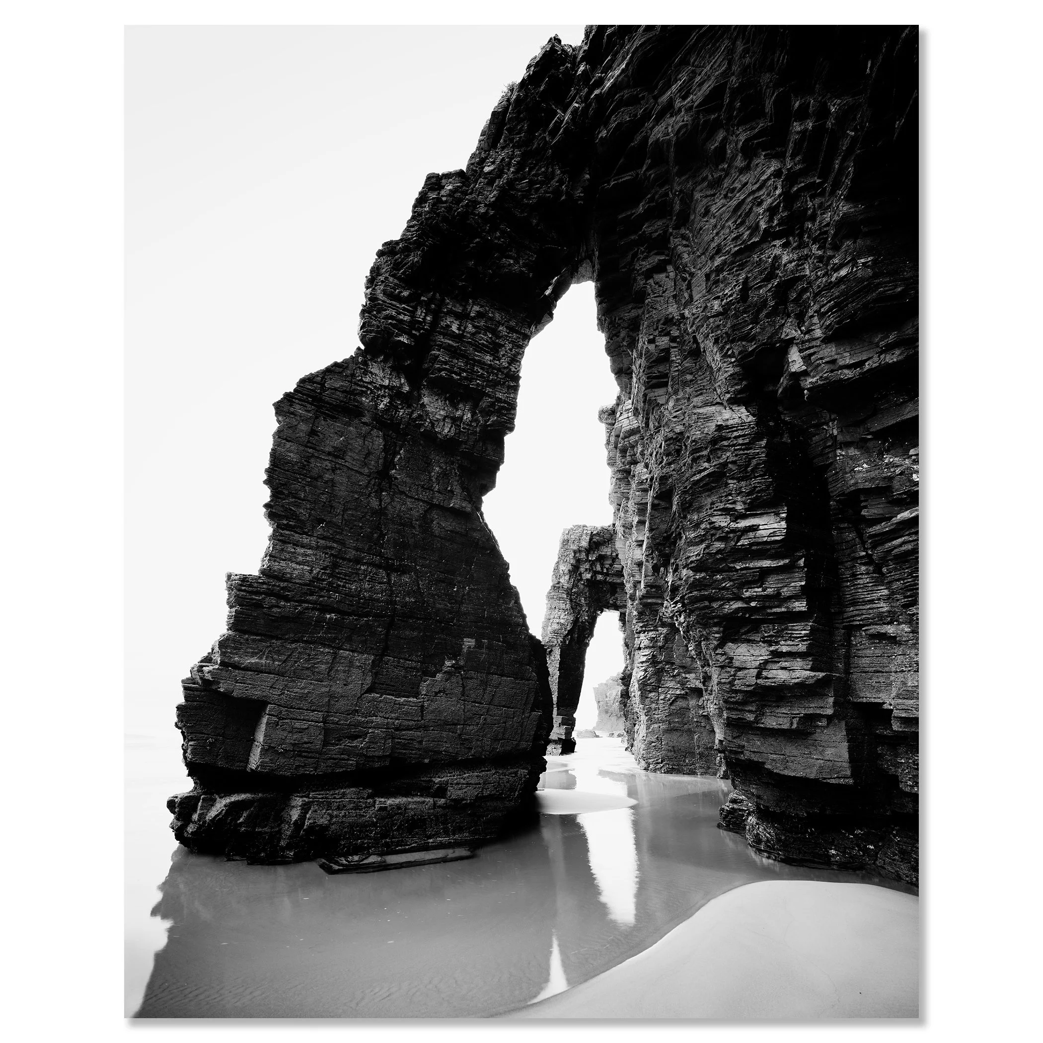 Black and white long-exposure minimalist seascape of rock arches on a beach with wet sand reflections – dibond frameless