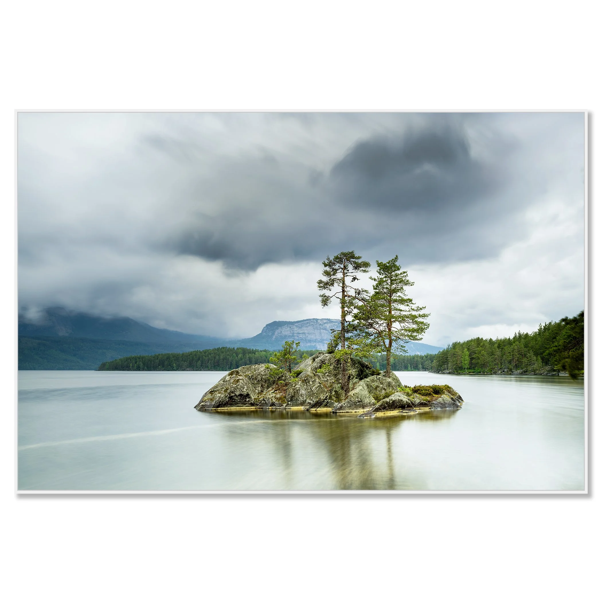 Gerald Berghammer - Color Photography. A small rocky island with tall pine trees surrounded by a calm lake under a cloudy sky and mountains behind. Chromaluxe framed white