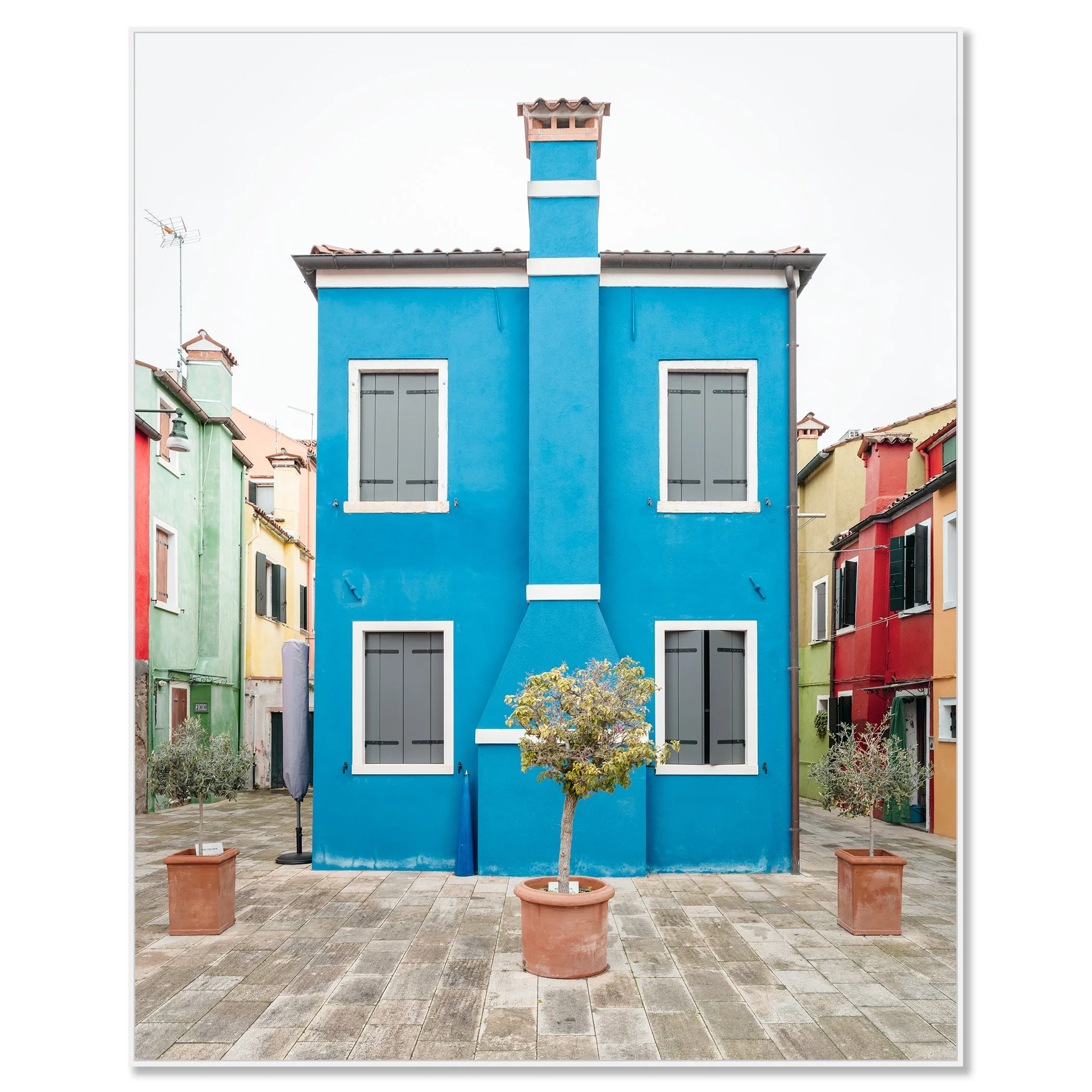© 2025 Gerald Berghammer - Color cityscape photo. Colorful row houses with a prominent blue house in the center, potted small trees in front, and a paved courtyard. Chromaluxe framed white