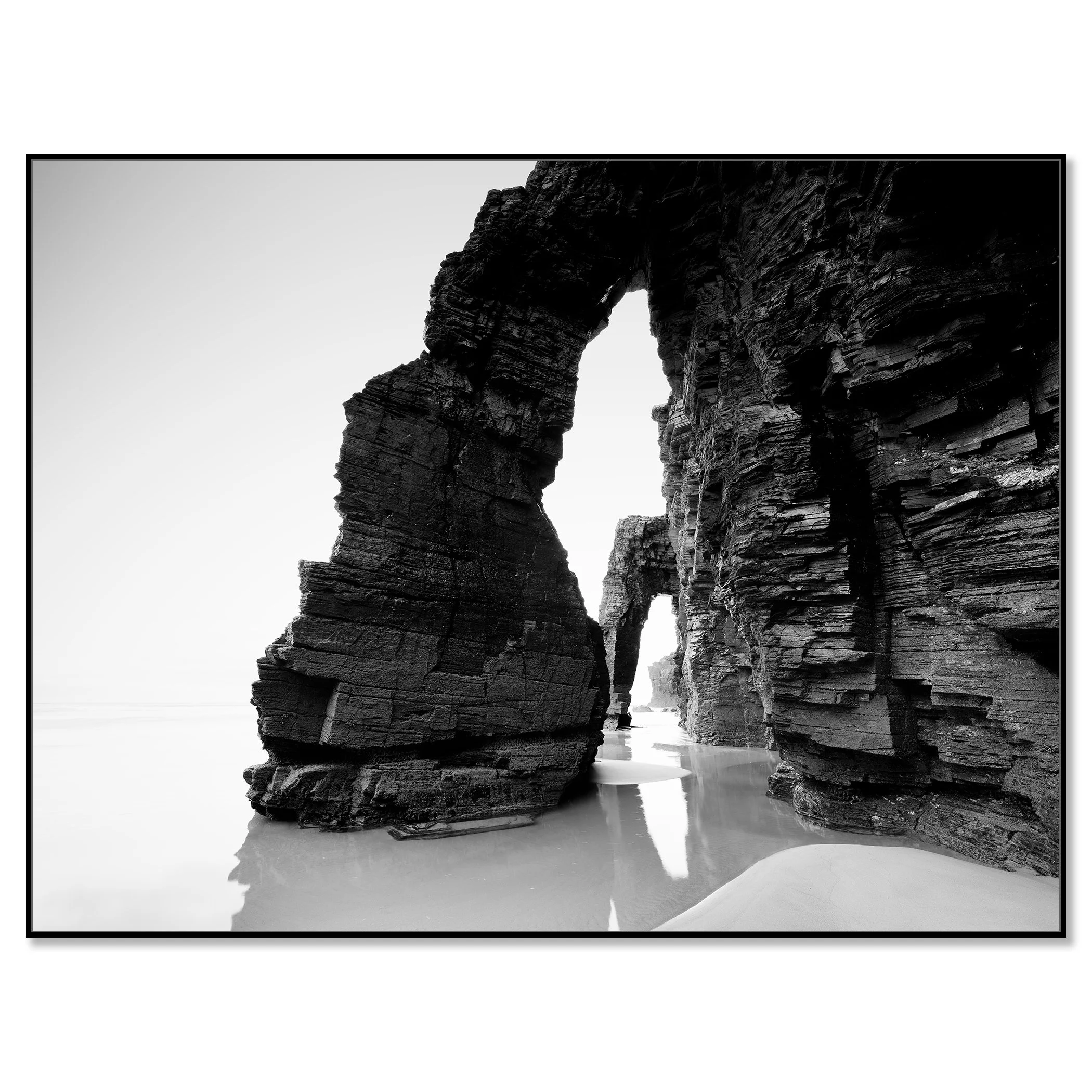 Gerald Berghammer - Black and white beach seascape photography. Large natural rock arch formations on a beach with water reflecting the rocks. Chromaluxe framed black