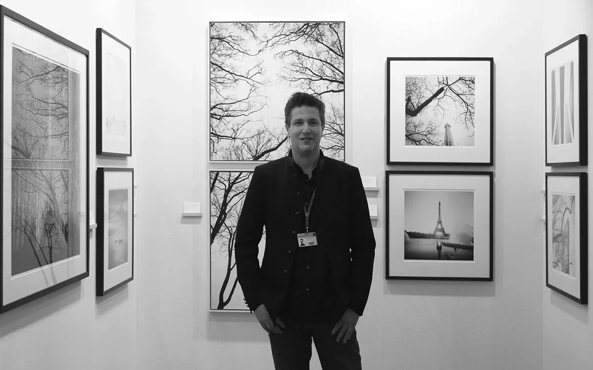 Gerald Berghammer standing in front of his framed black-and-white fine art photographs at art KARLSRUHE 2018.