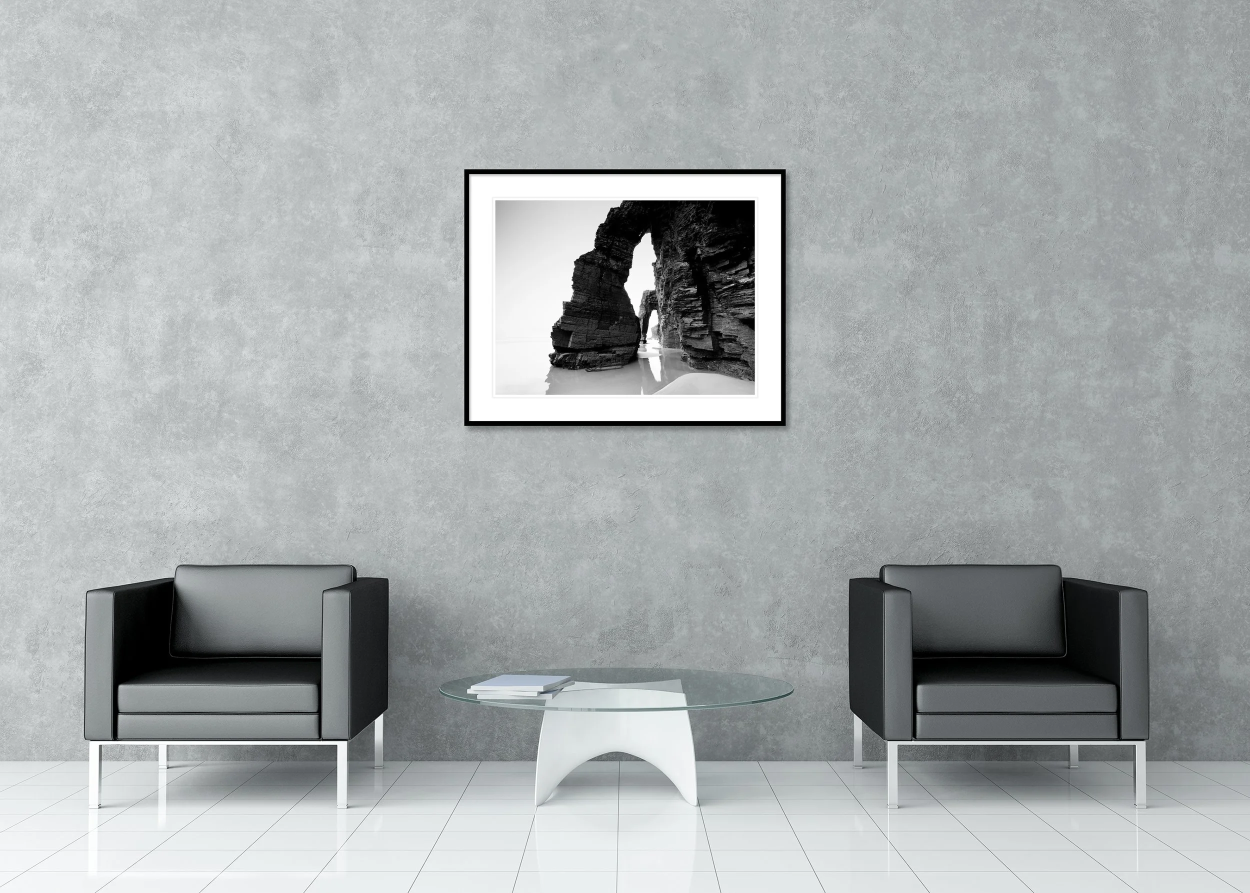 Fine art black and white seascape photo of rock arch formations on the beach, reflected in tidal water, as an archival pigment print in a classic frame with a mount.