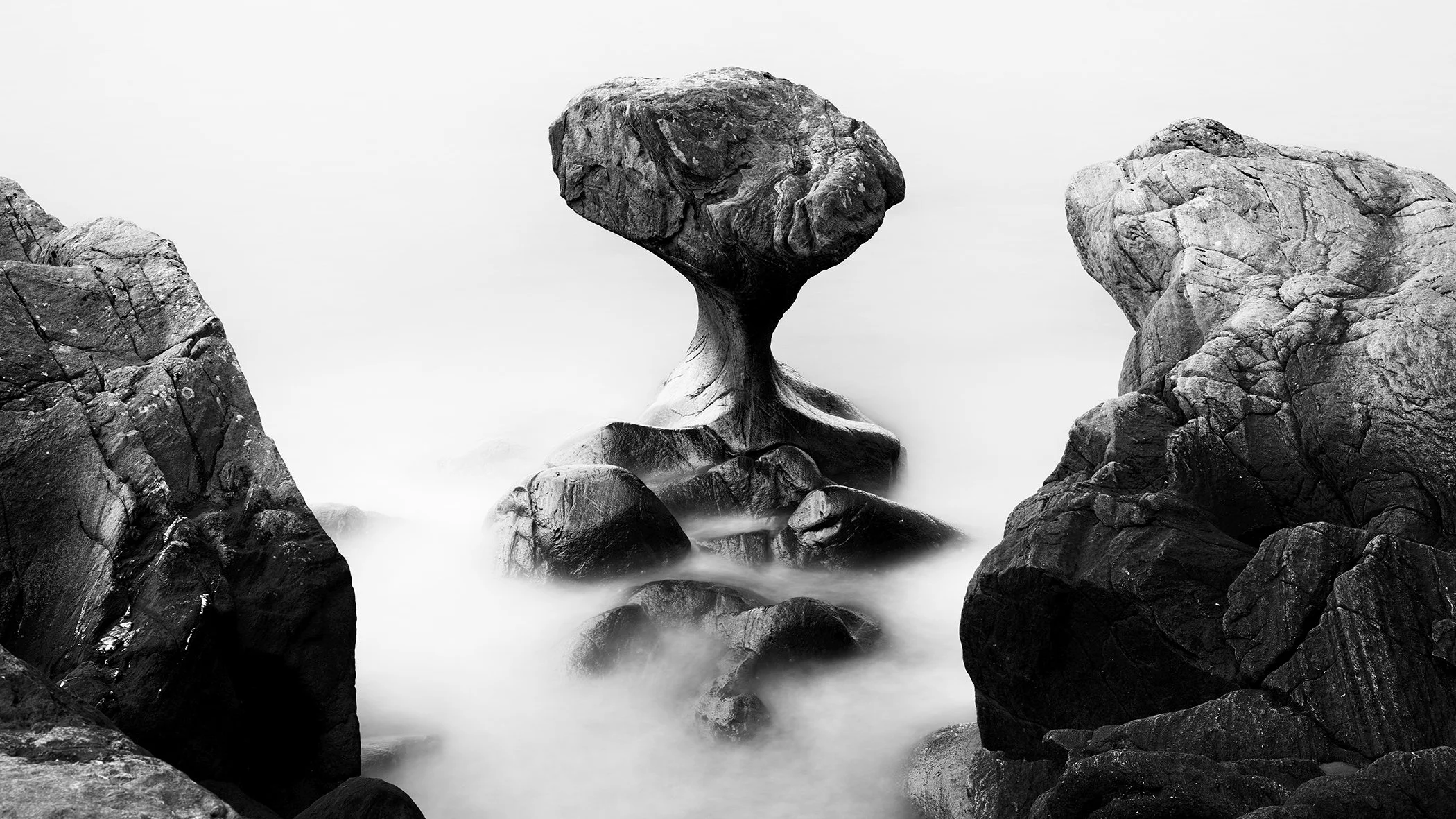 Balanced boulders in water, creating a mushroom-like rock formation in a minimalist landscape scene