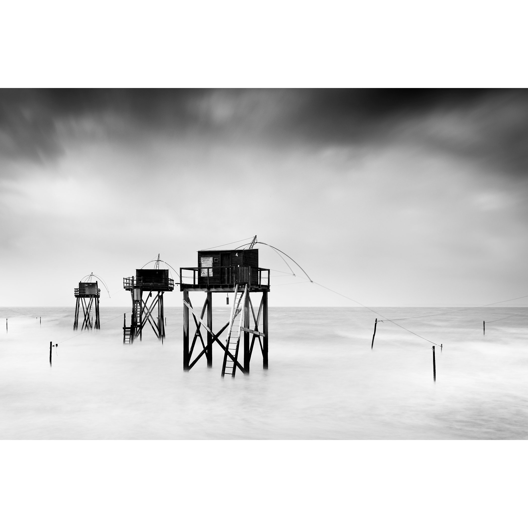 Monochrome long-exposure seascape with wooden fishing huts on stilts and misty water