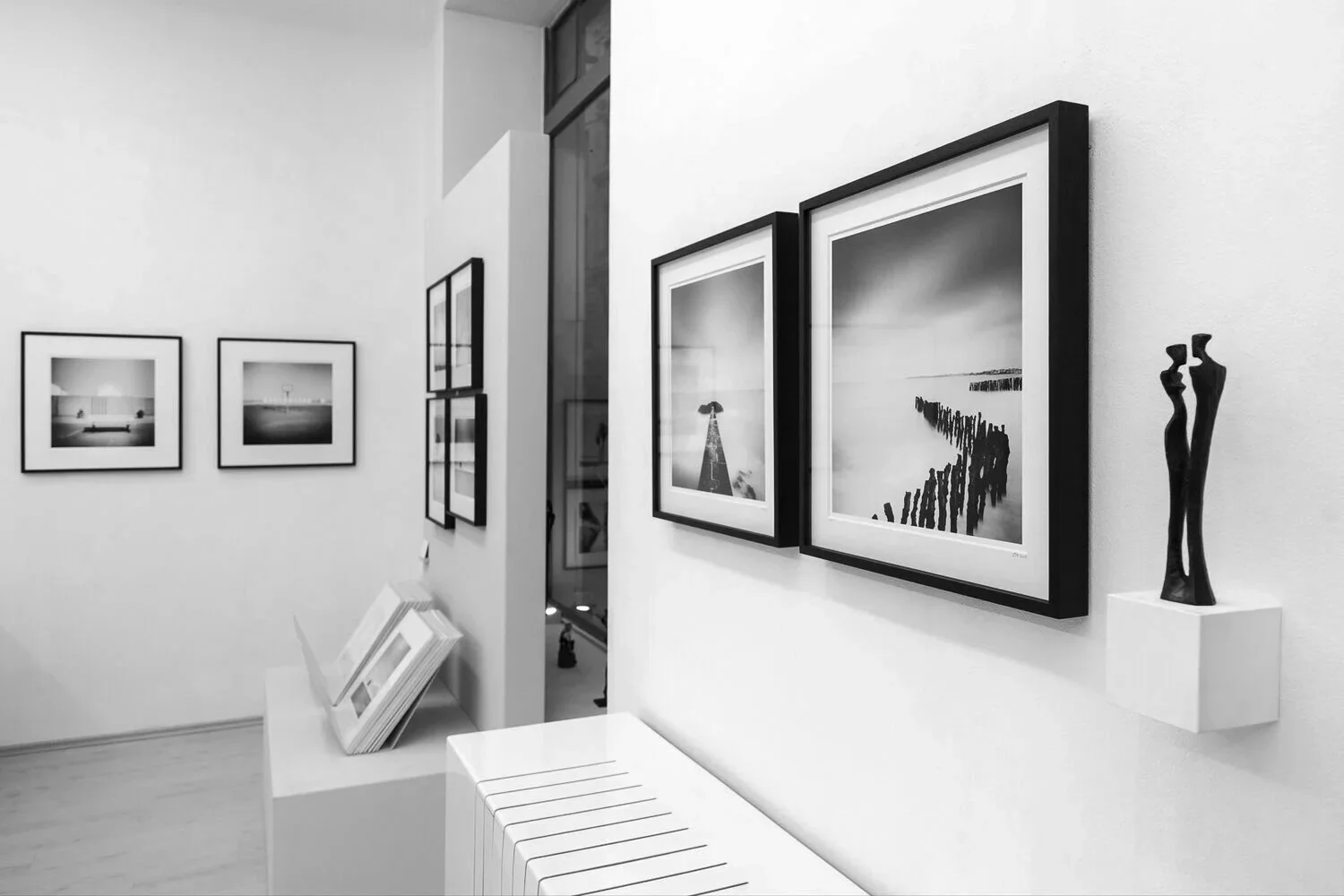 Black-and-white coastal photographs by Gerald Berghammer displayed with figurative sculptures at SILVERFINEART Gallery.