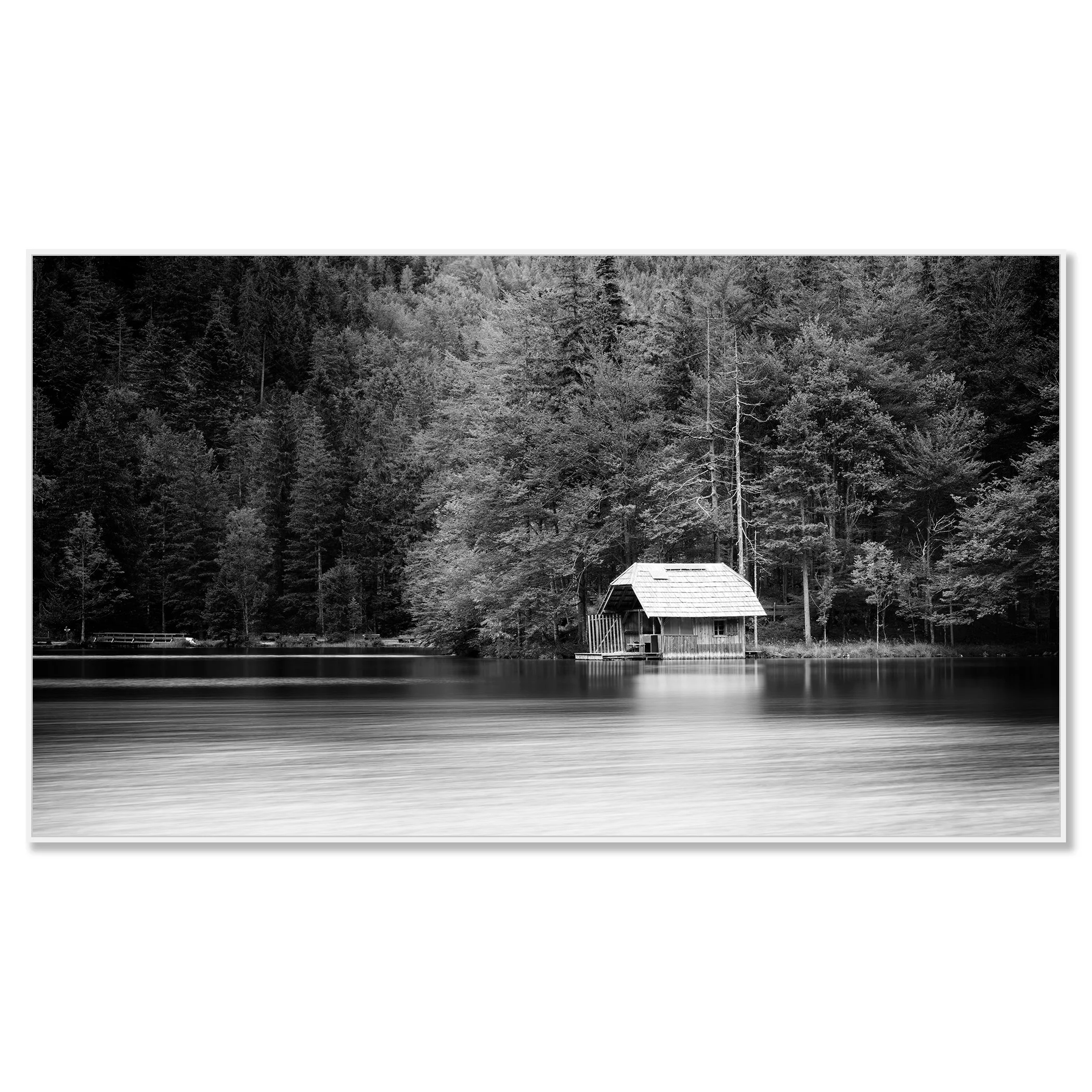 Calm lake in black and white with a small boathouse, wooden jetty and trees along the shore – framed ArtBox white