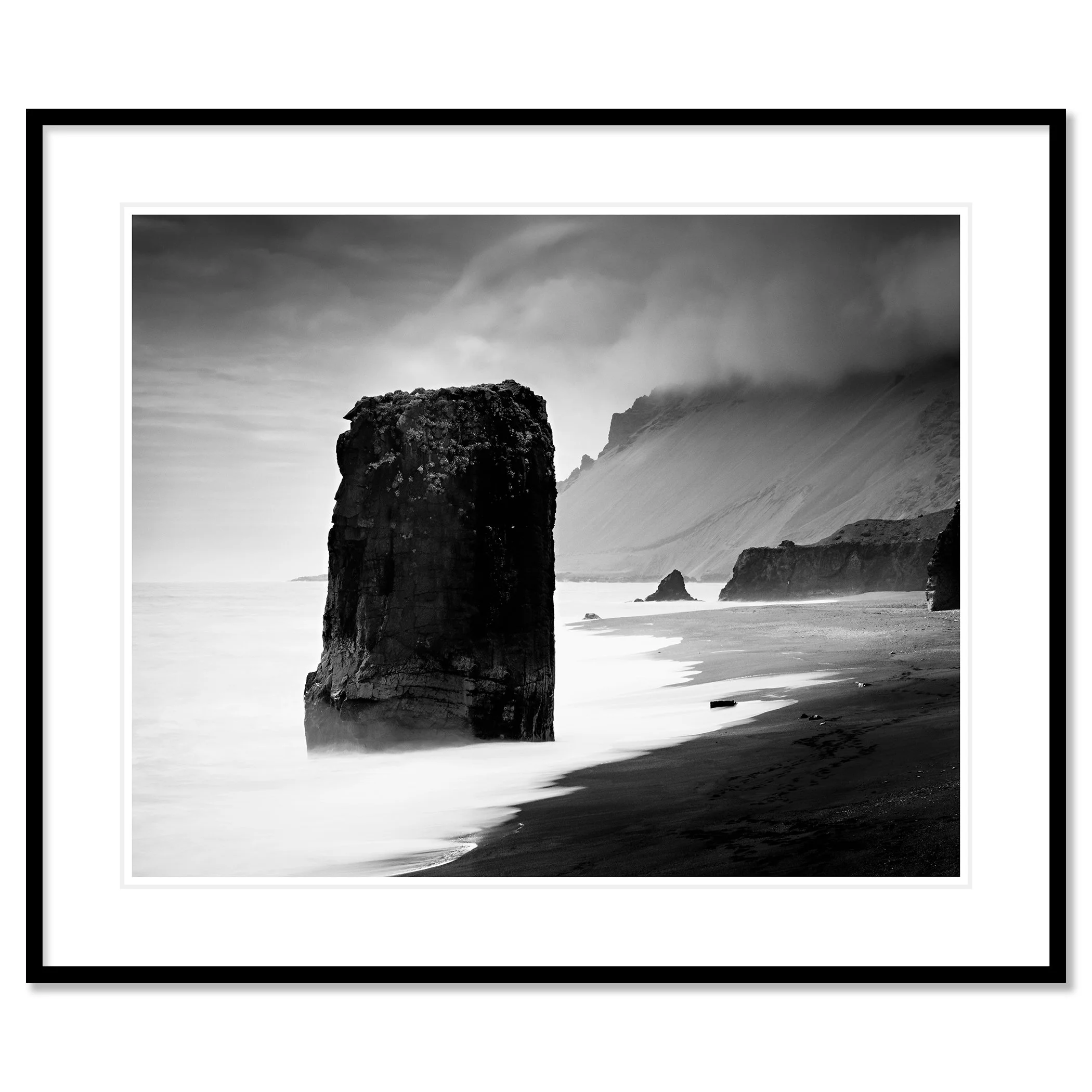 Gerald Berghammer - Black and white Photography. Coastal landscape featuring large sea stacks, sandy shoreline and cliffs with mist over the distant hills. Classic framed black
