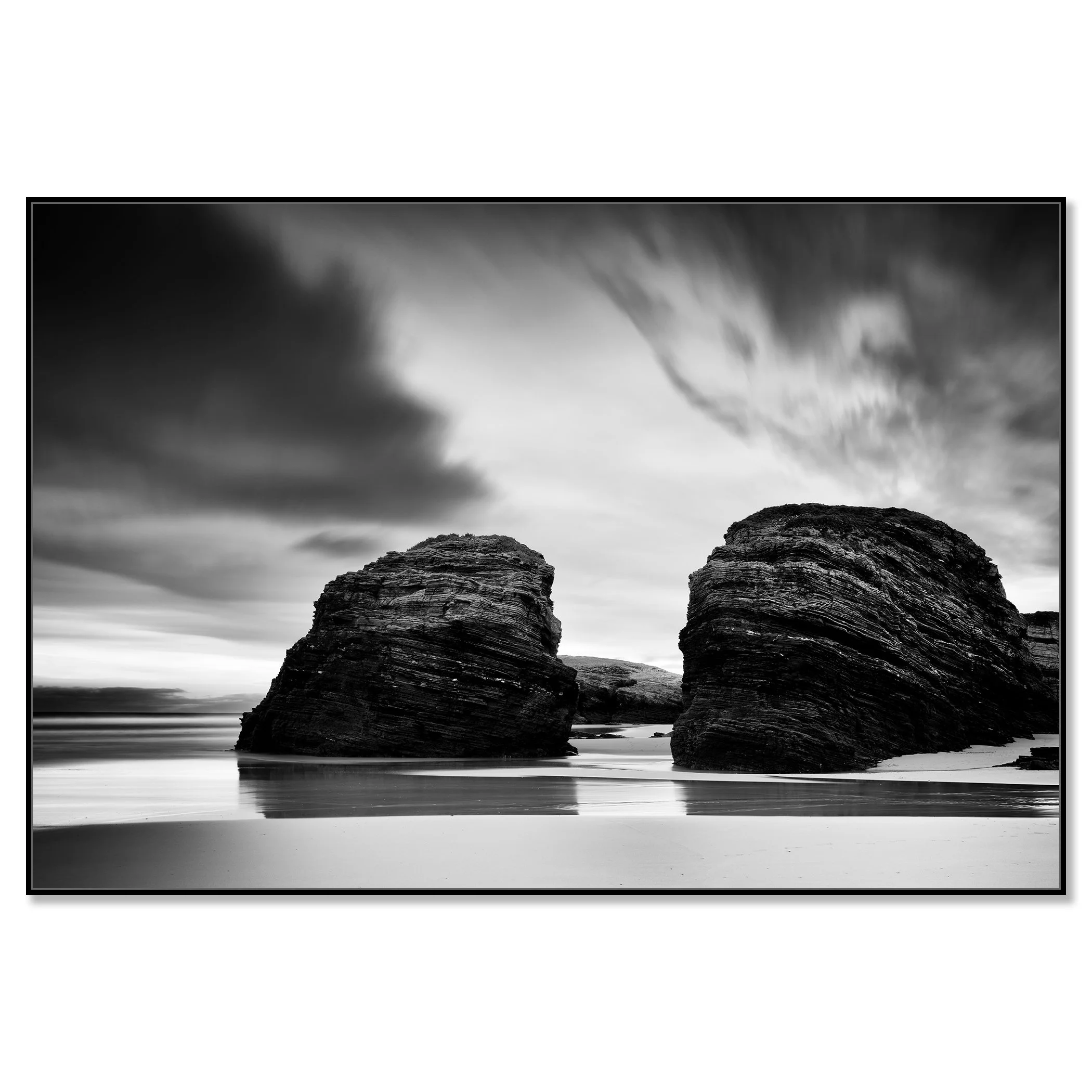 Black and white seascape with two rounded rocks on a beach beneath a cloudy sky – framed ArtBox black