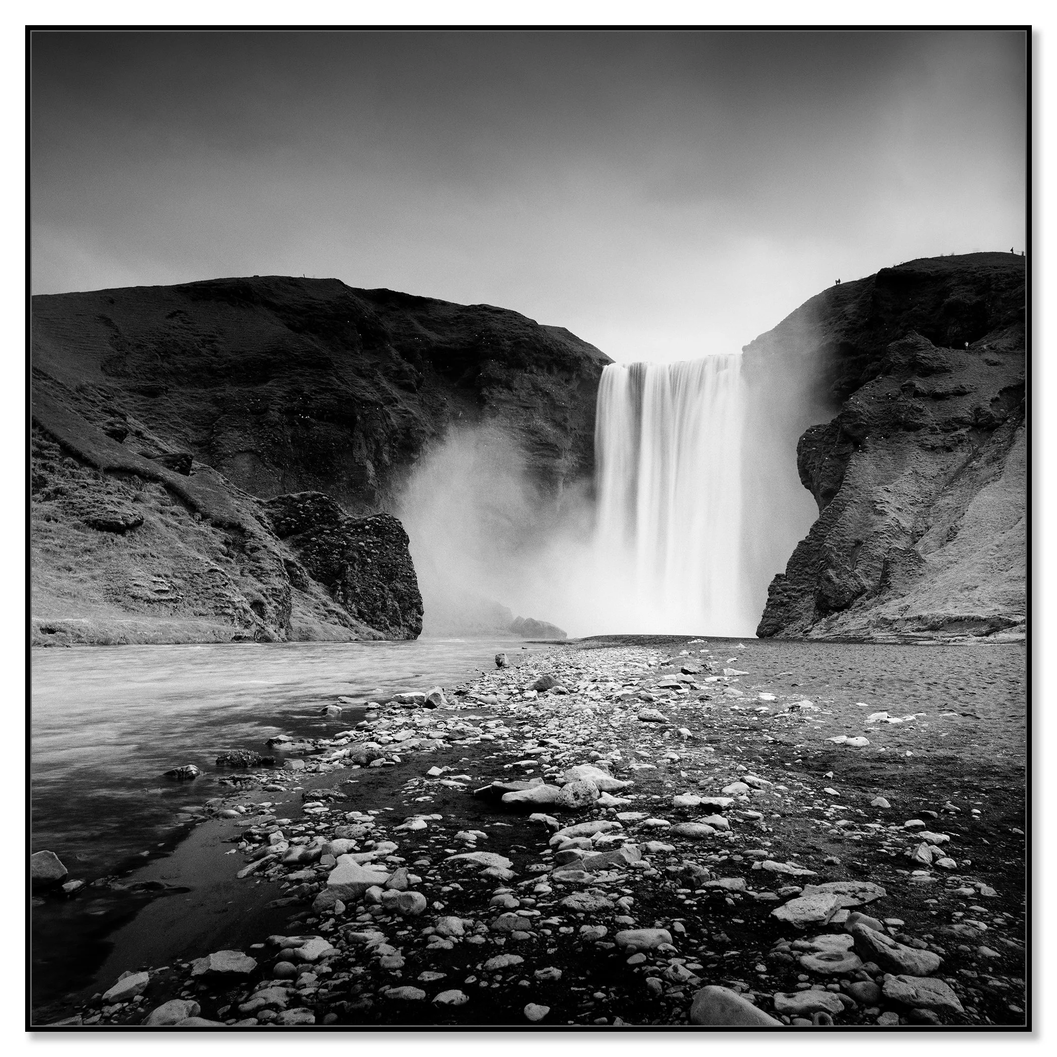Black and white long-exposure photo of a large waterfall between rugged cliffs into a rocky river – framed ArtBox black