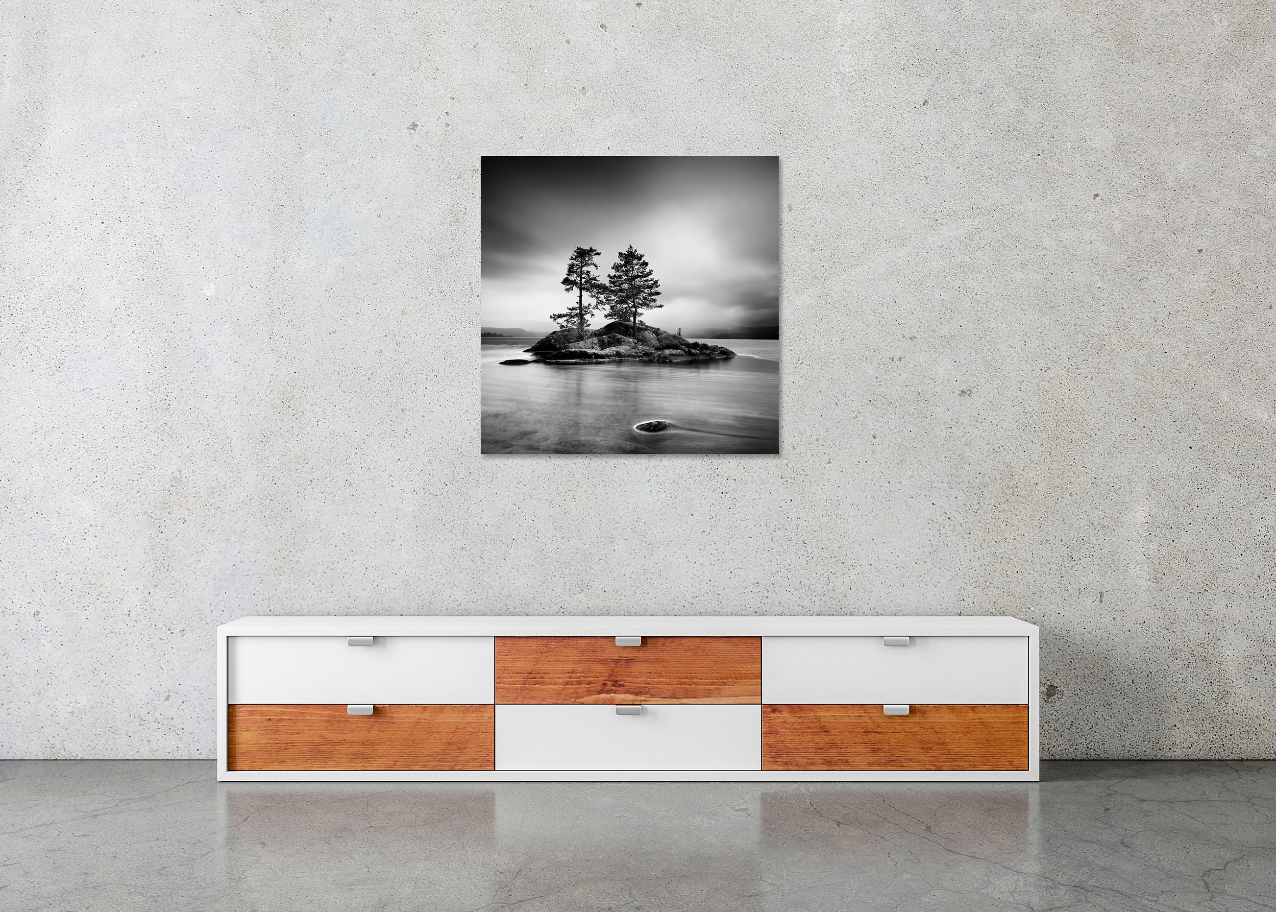 Black and white landscape print of two pine trees on a rocky island in a calm lake under a cloudy sky, mounted to Dibond, frameless
