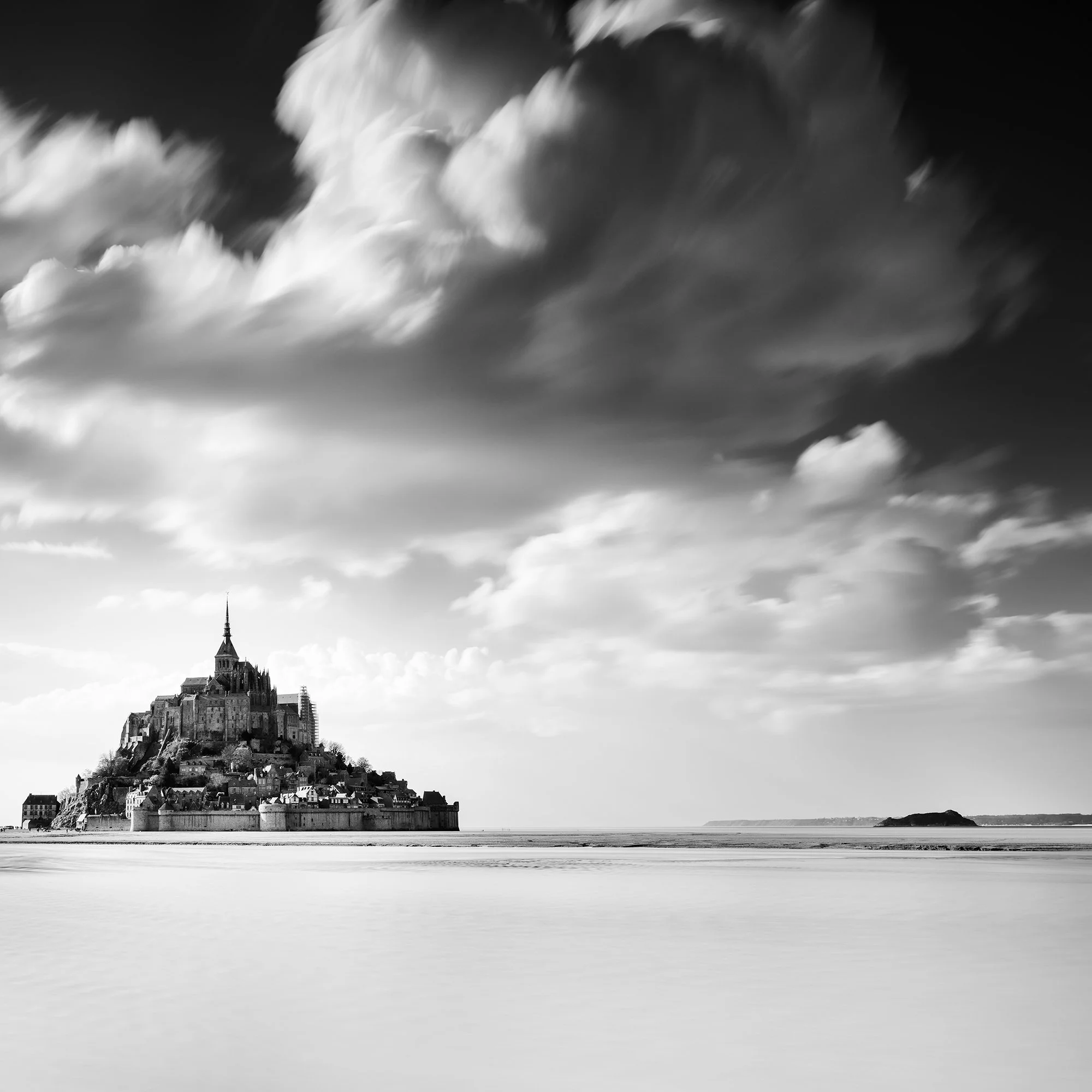 © 2023 Gerald Berghammer - B&W photography. Mont Saint-Michel, a historic island with a tall spire and medieval architecture, surrounded by water and clouds. Print detail 2