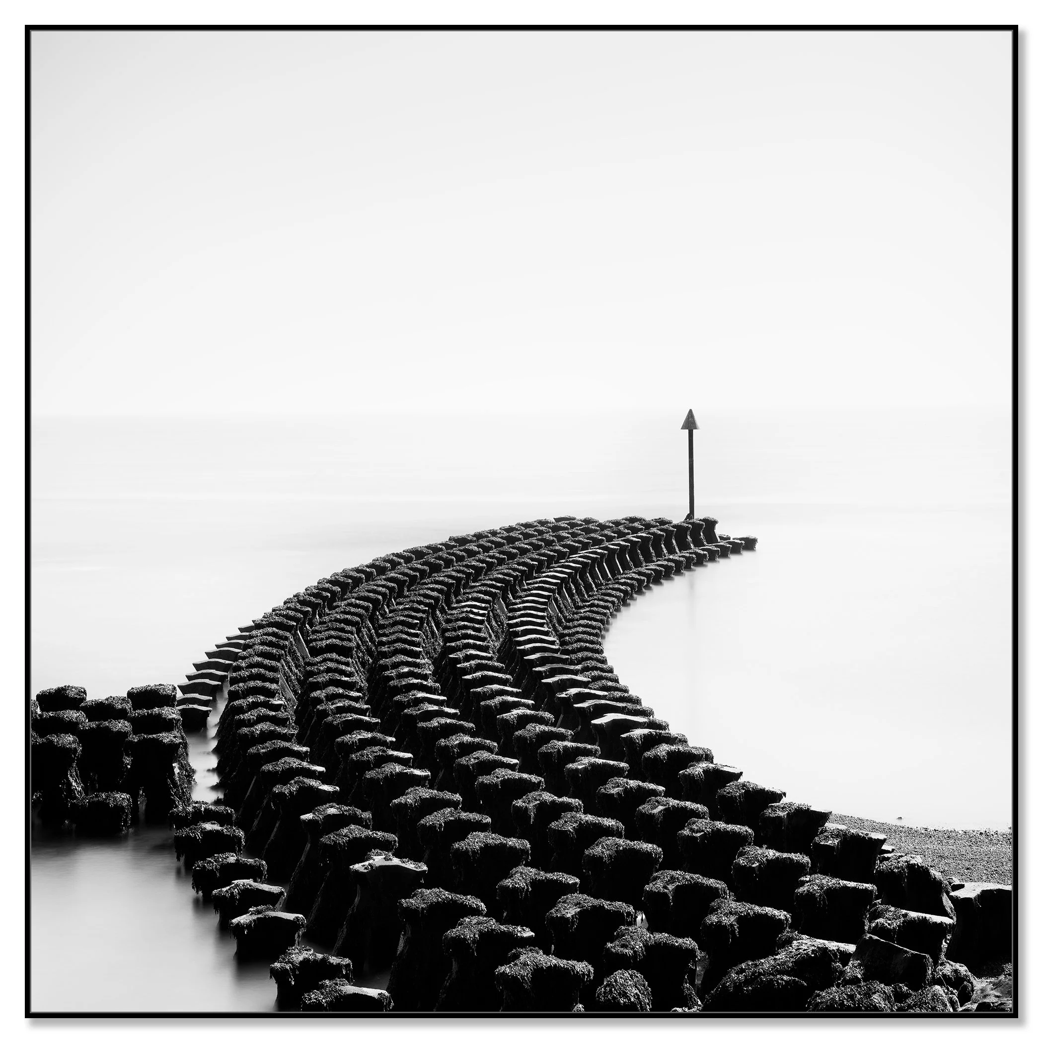 Black and white seascape with curved timber groynes leading to a coastal warning sign – framed ArtBox black