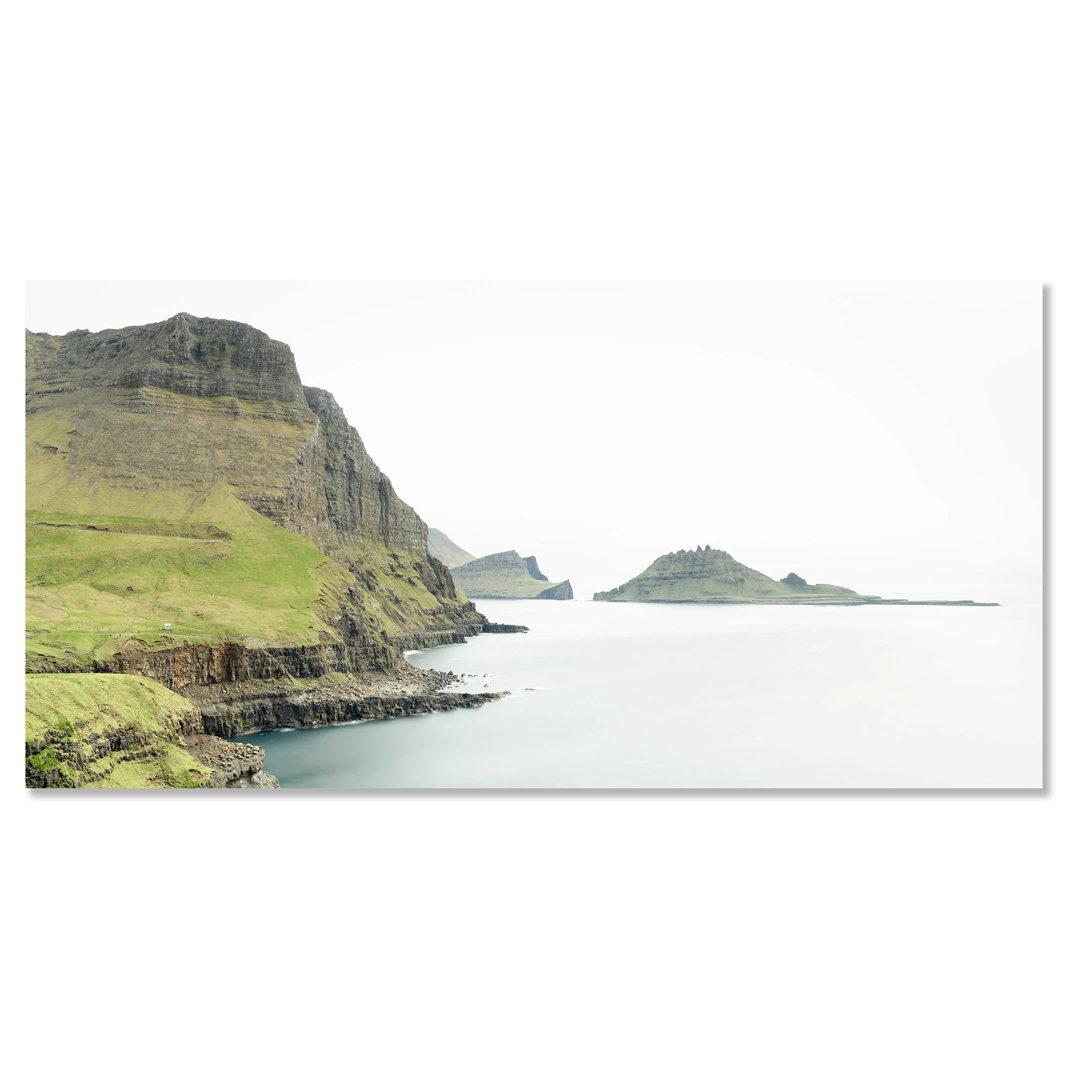 Gerald Berghammer - Color Photography. Cliffs and green hills along a body of water, with distant islands or landmasses in the background under a cloudy sky. Chromaluxe frameless
