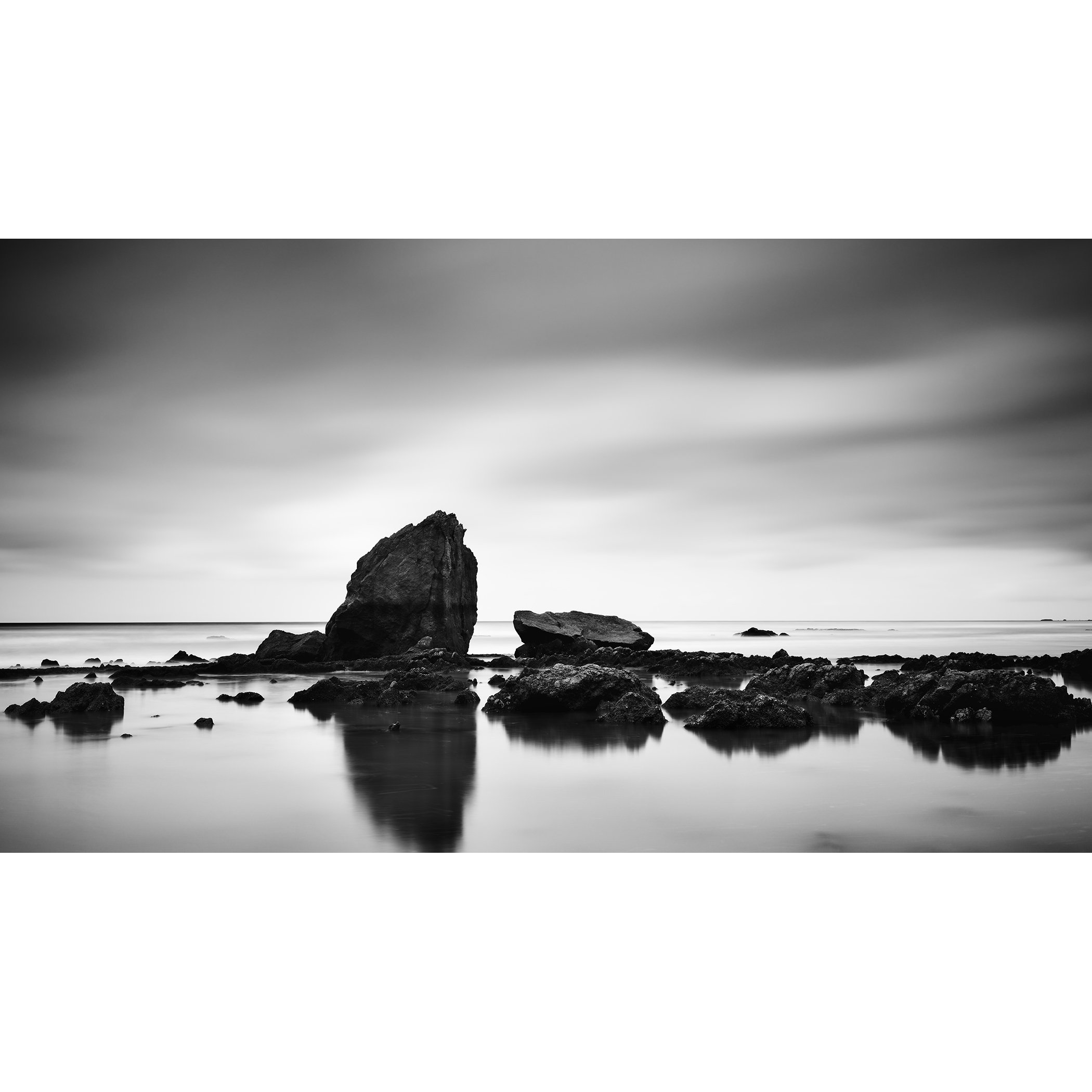 © 2023 Gerald Berghammer - Black and white minimalist beach seascape. A rocky shoreline with a large prominent rock formation in the water.